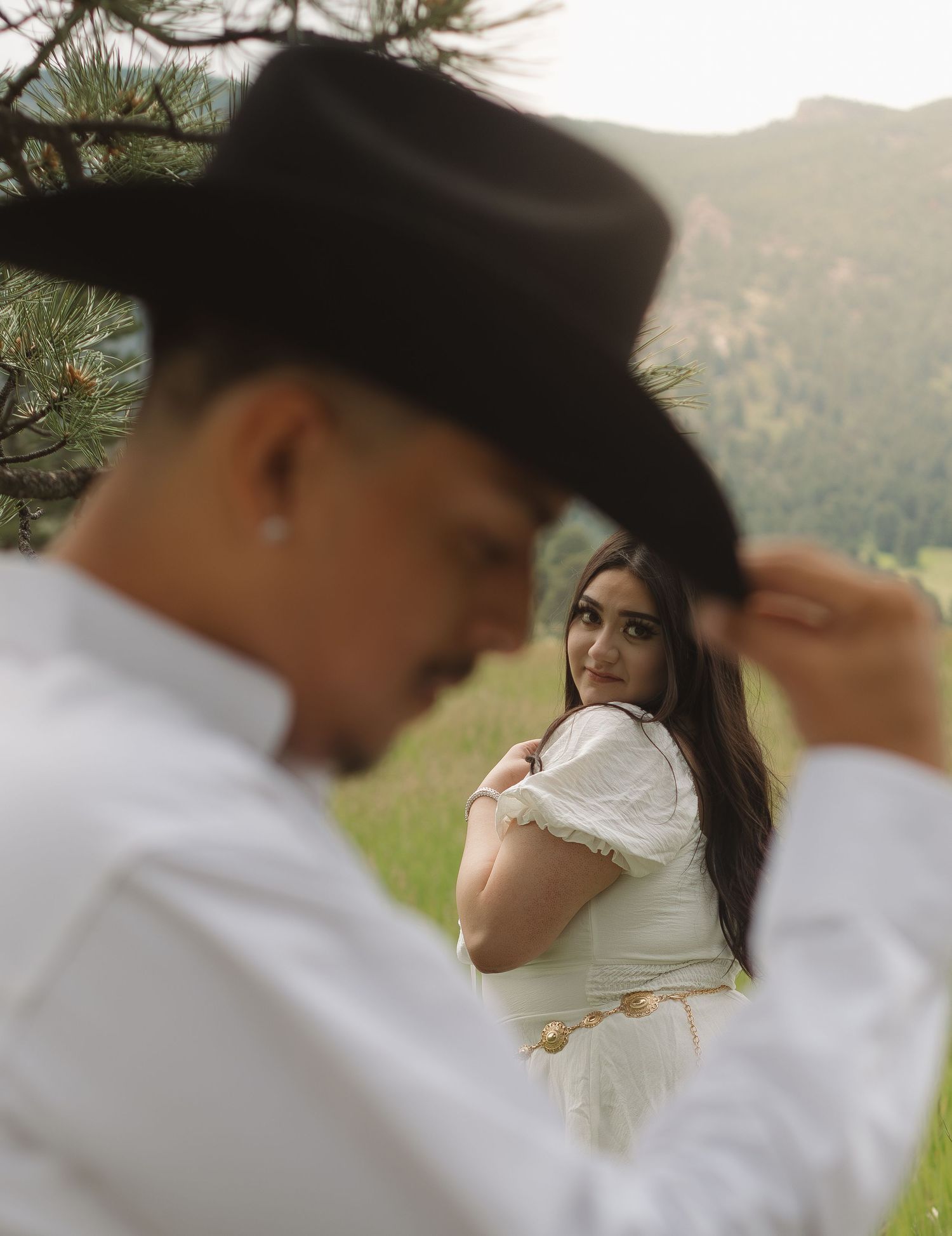 A couple in western-inspired outfits poses romantically in a mountain meadow setting.