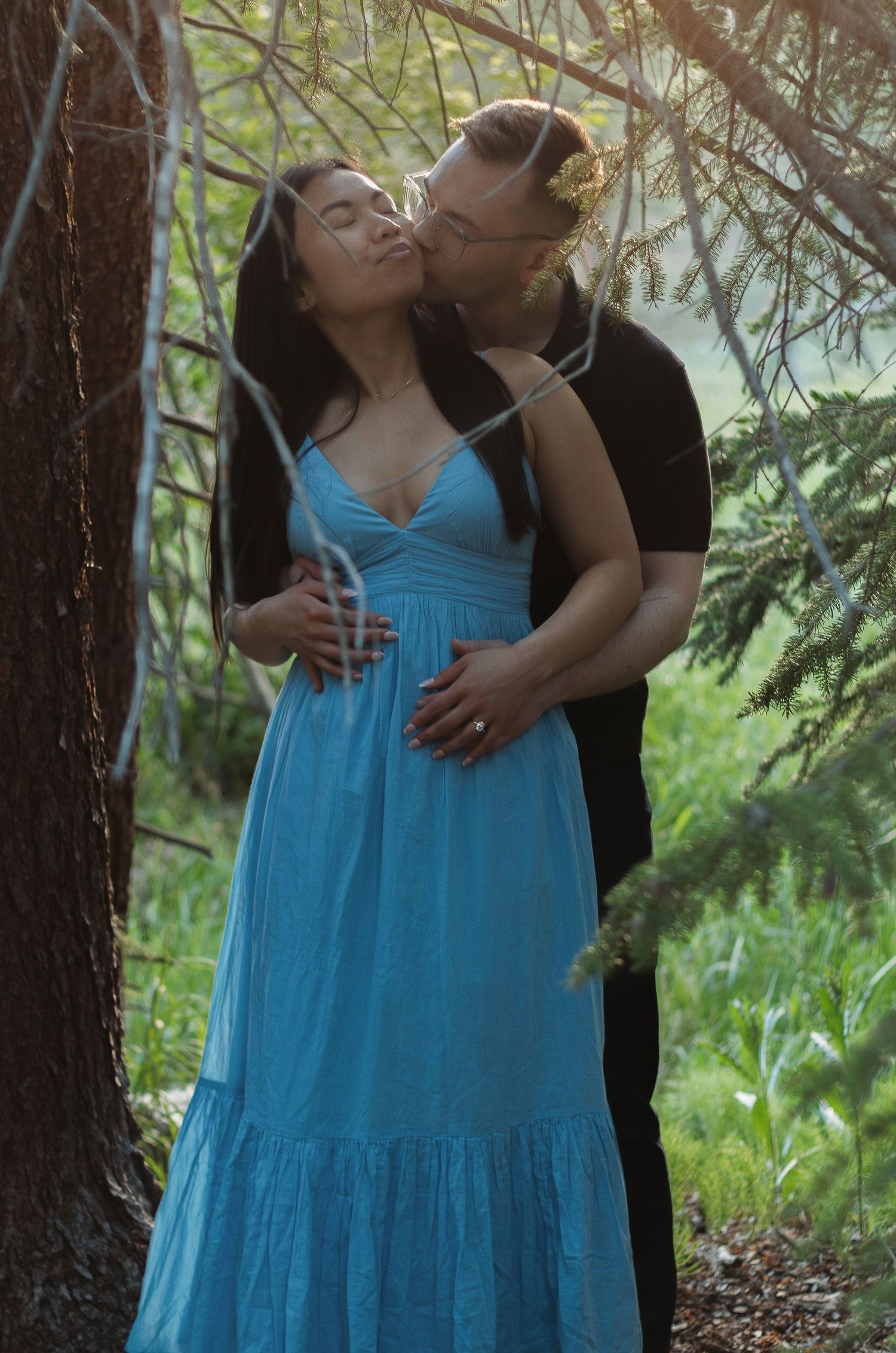 Romantic moment captured in a forest setting with blue dress and natural lighting.
