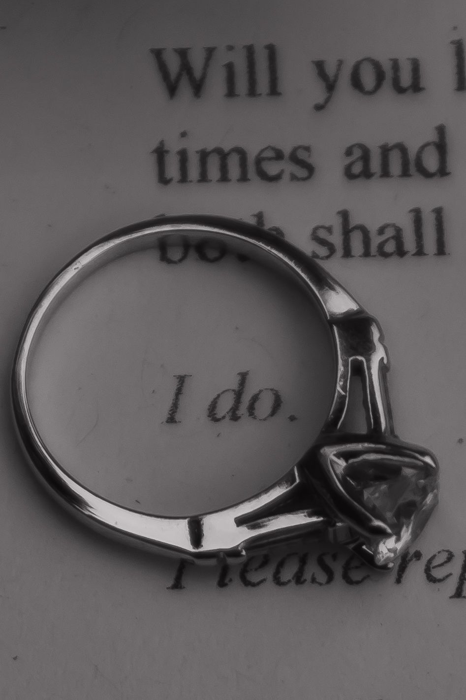 Black and white photograph of engagement rings with the words 'I do' visible in the background.