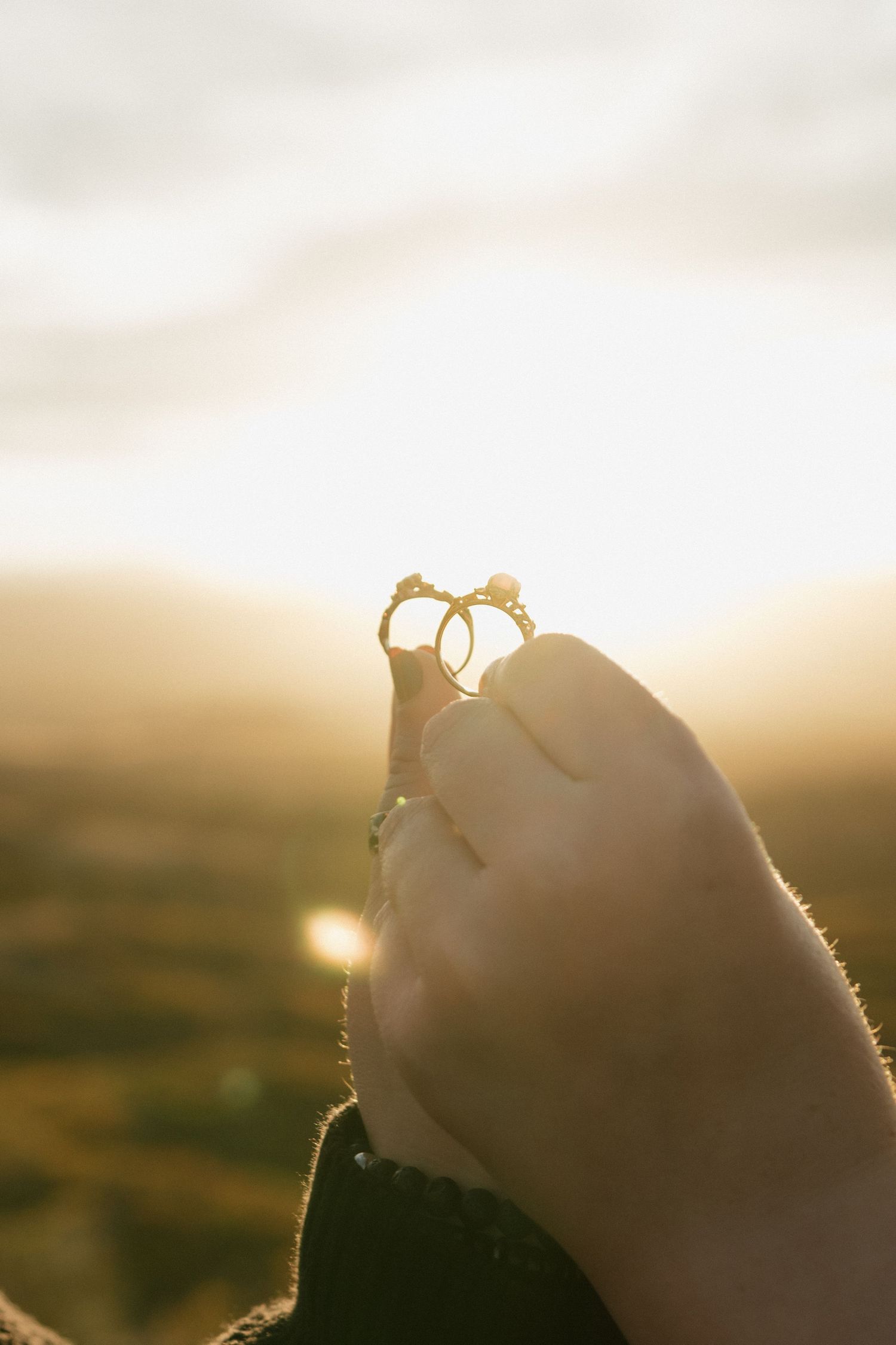 Hand holding a ring against a golden sunset sky with sunlight creating a silhouetted backlit effect.