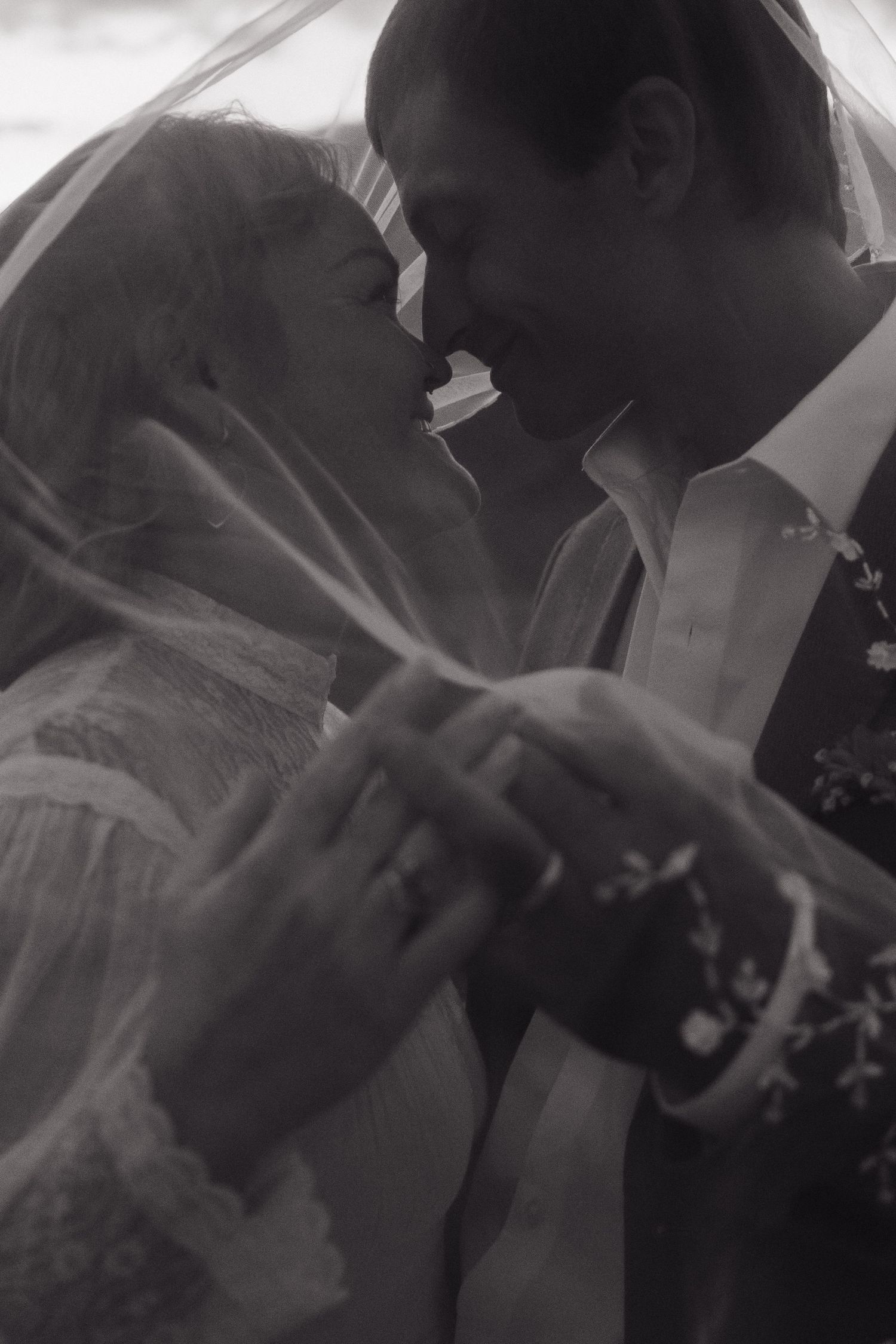 Black and white photo of bride and groom sharing romantic moment under wedding veil.