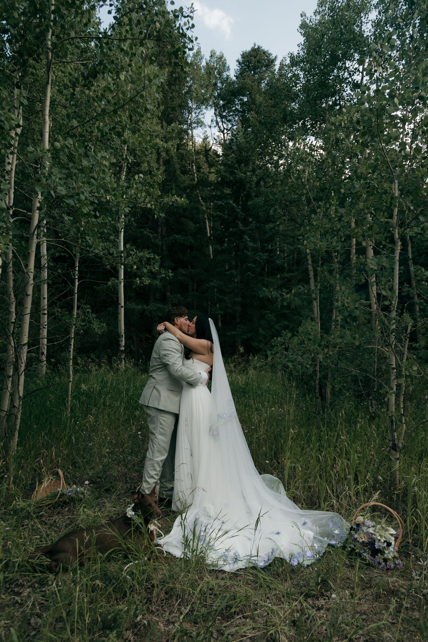 Bride and groom share first kiss surrounded by tall aspen trees in a forest elopement.