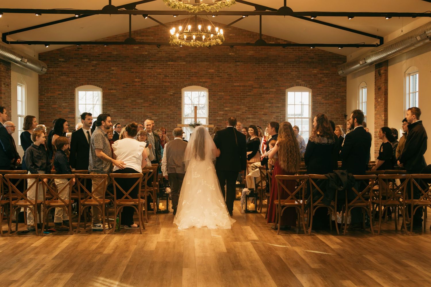 Wedding ceremony in a rustic brick venue with exposed beams and elegant chandelier lighting.
