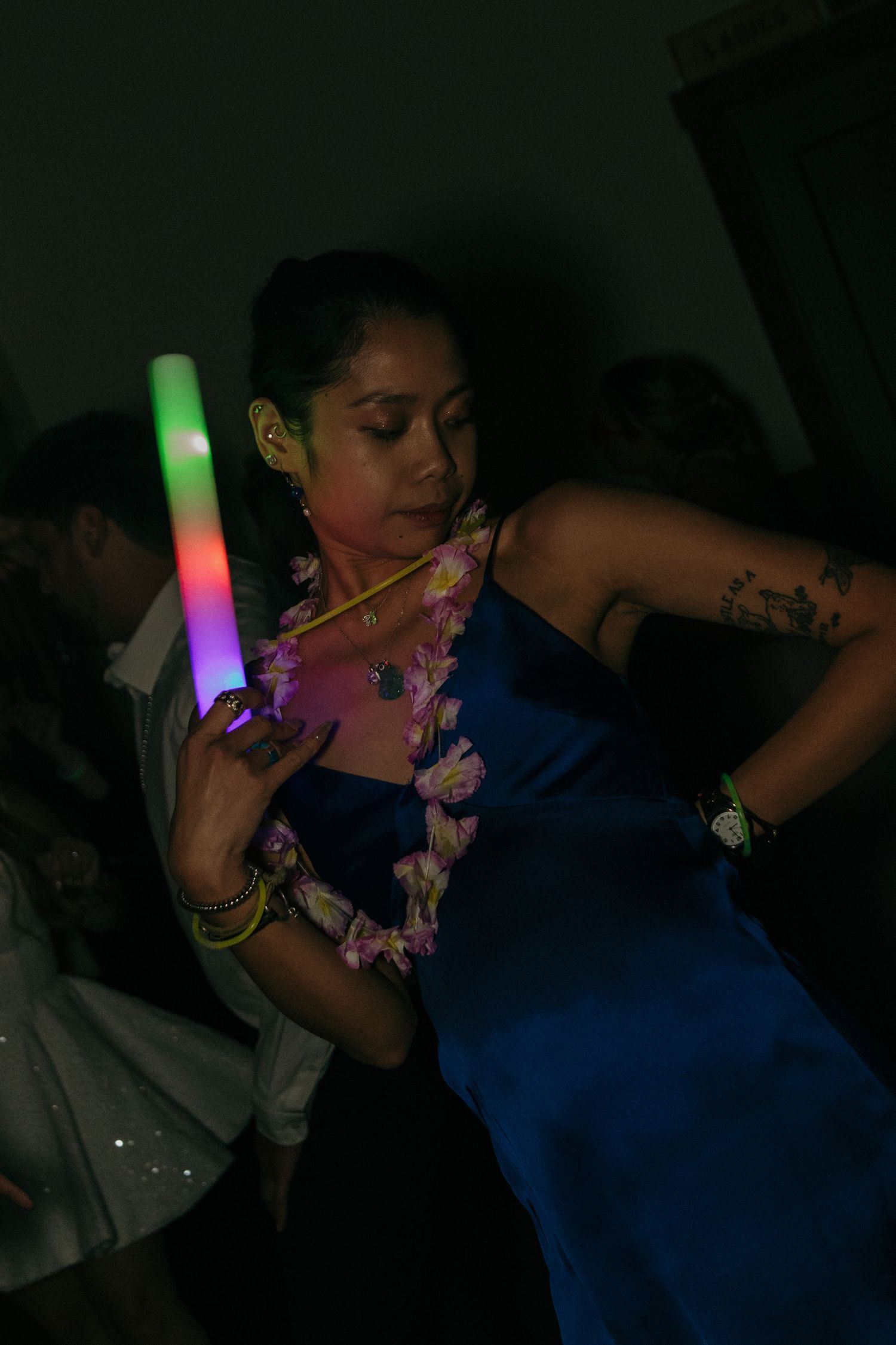 Party guests dancing with colorful LED glow sticks in dark reception venue.