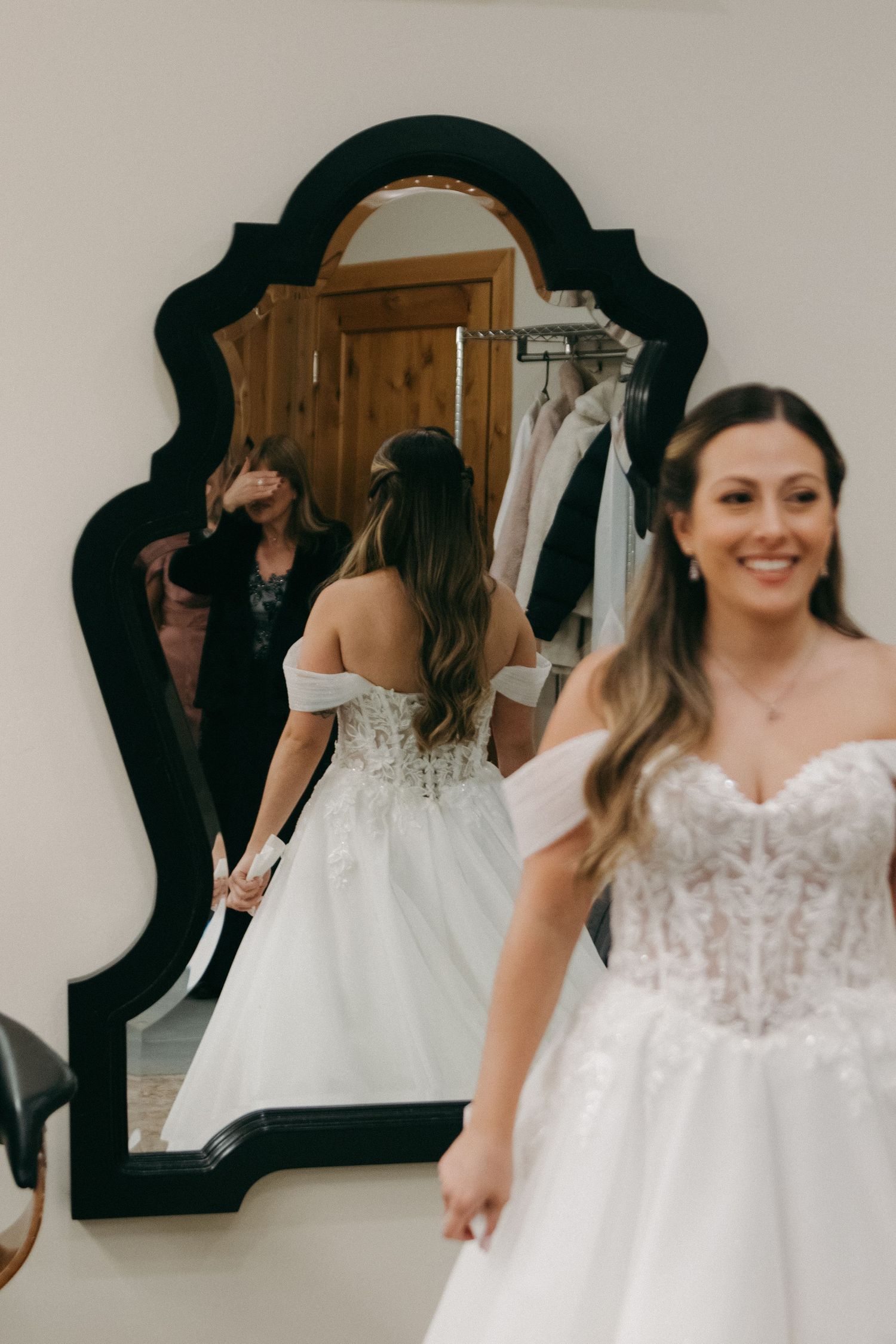Wedding dress fitting session reflected in an ornate black-framed mirror.