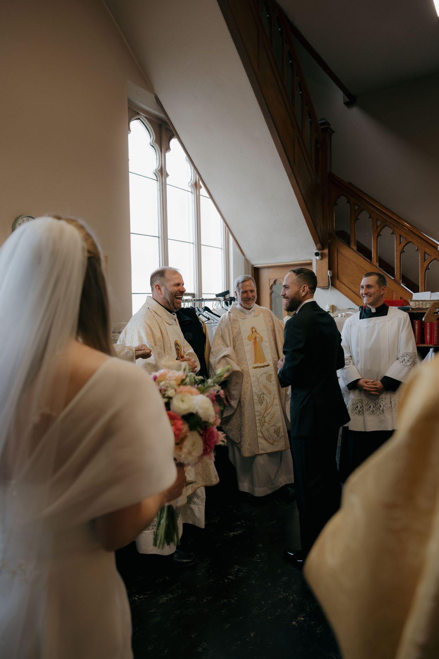 Groom laughing with priests inside church before wedding ceremony begins.