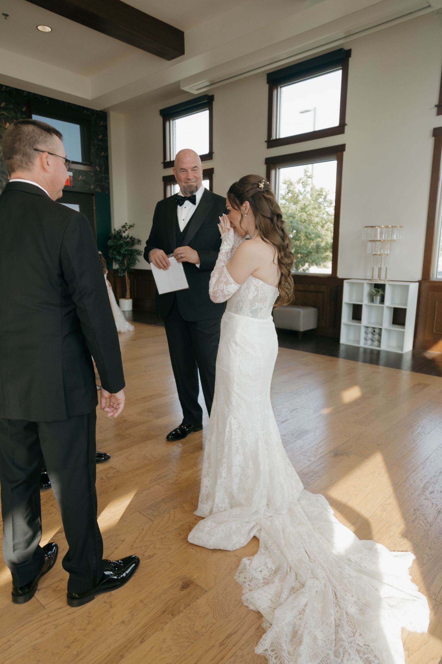 Emotional bride wiping tears during indoor wedding rehearsal with groom and officiant in elegant venue.