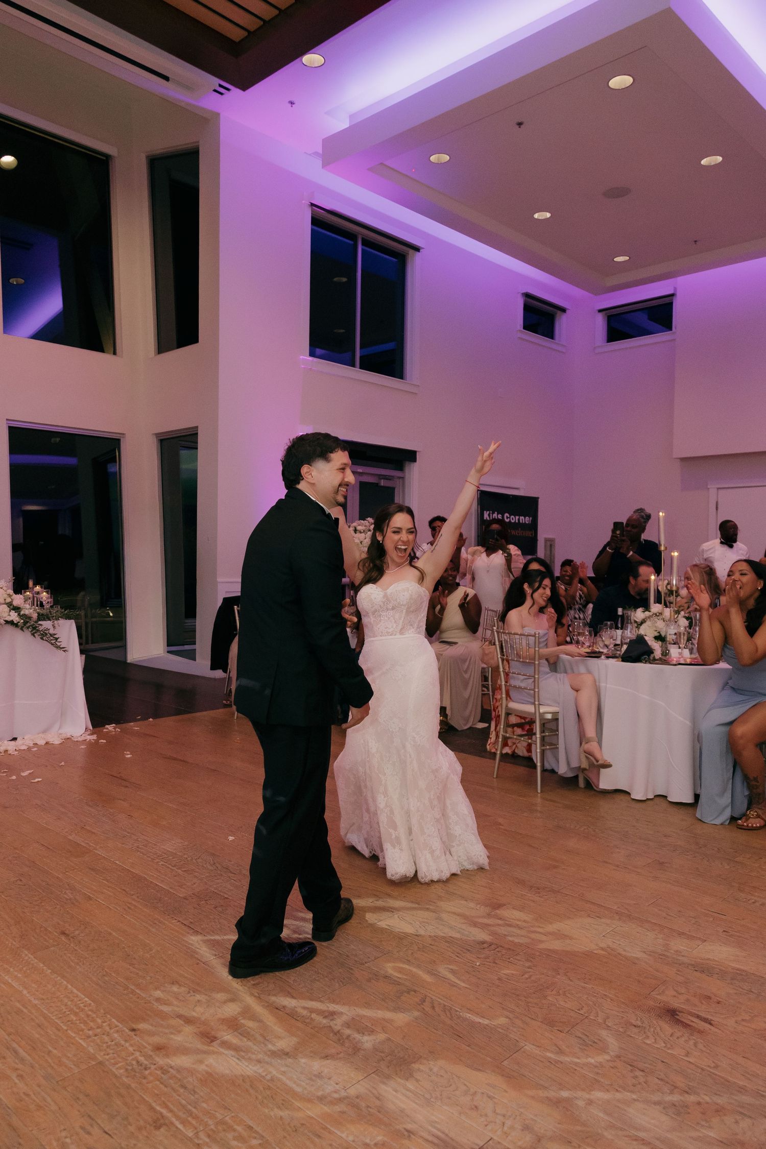 Bride and groom share first dance in elegant reception hall with purple uplighting.