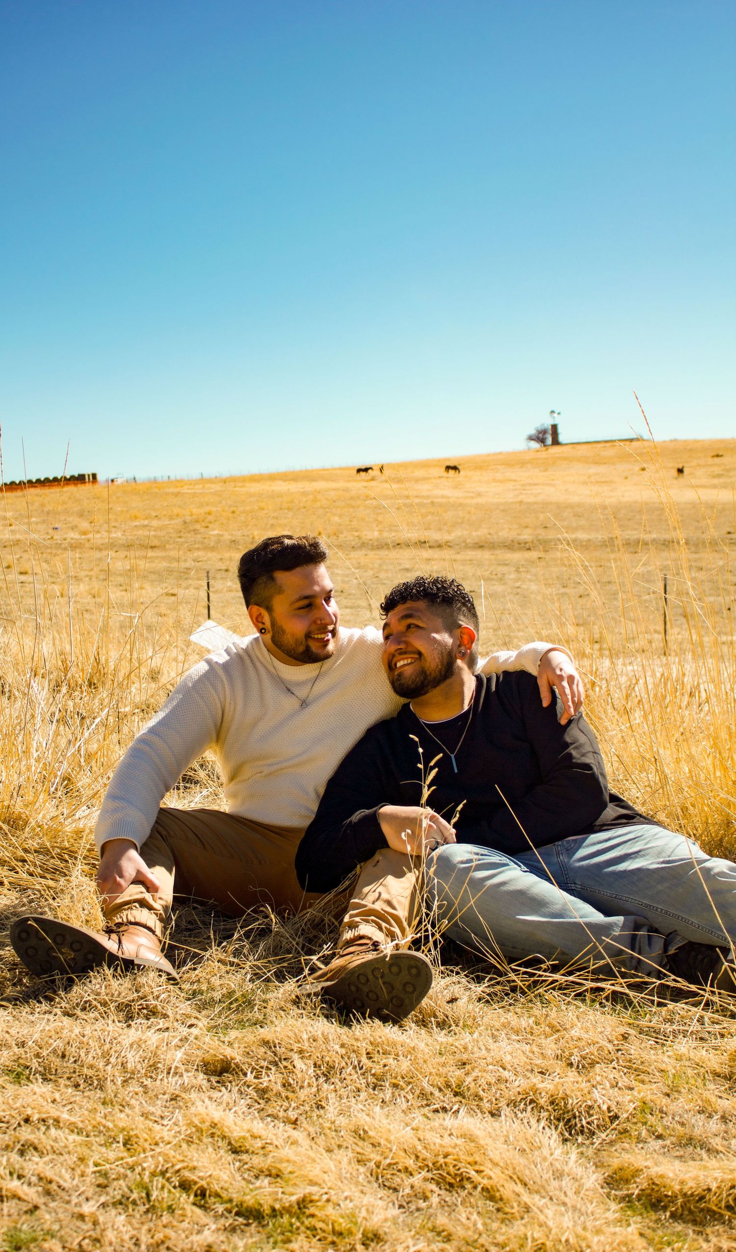 A couple relaxing together in a sun-dried grass field with blue sky overhead.