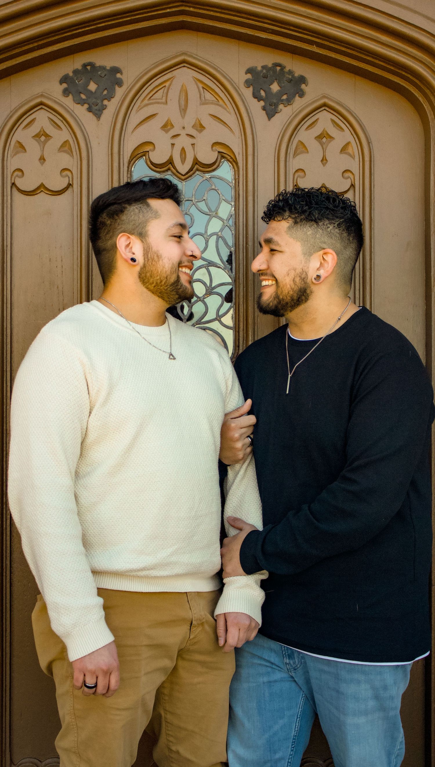 A couple in casual sweaters sharing an intimate moment in front of an ornate Gothic doorway.