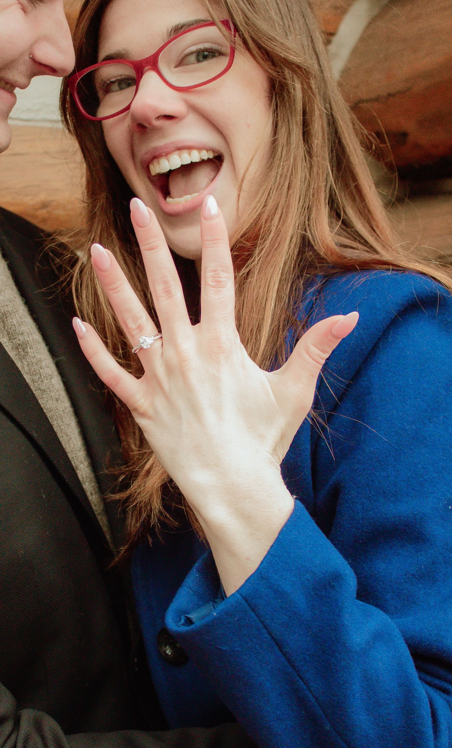 A close-up shot showing a hand with a new engagement ring against a bright blue coat.