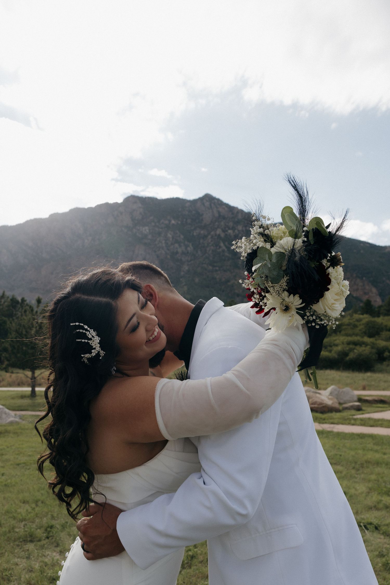 Bride and groom embracing in front of rocky mountain landscape holding black and white bouquet.