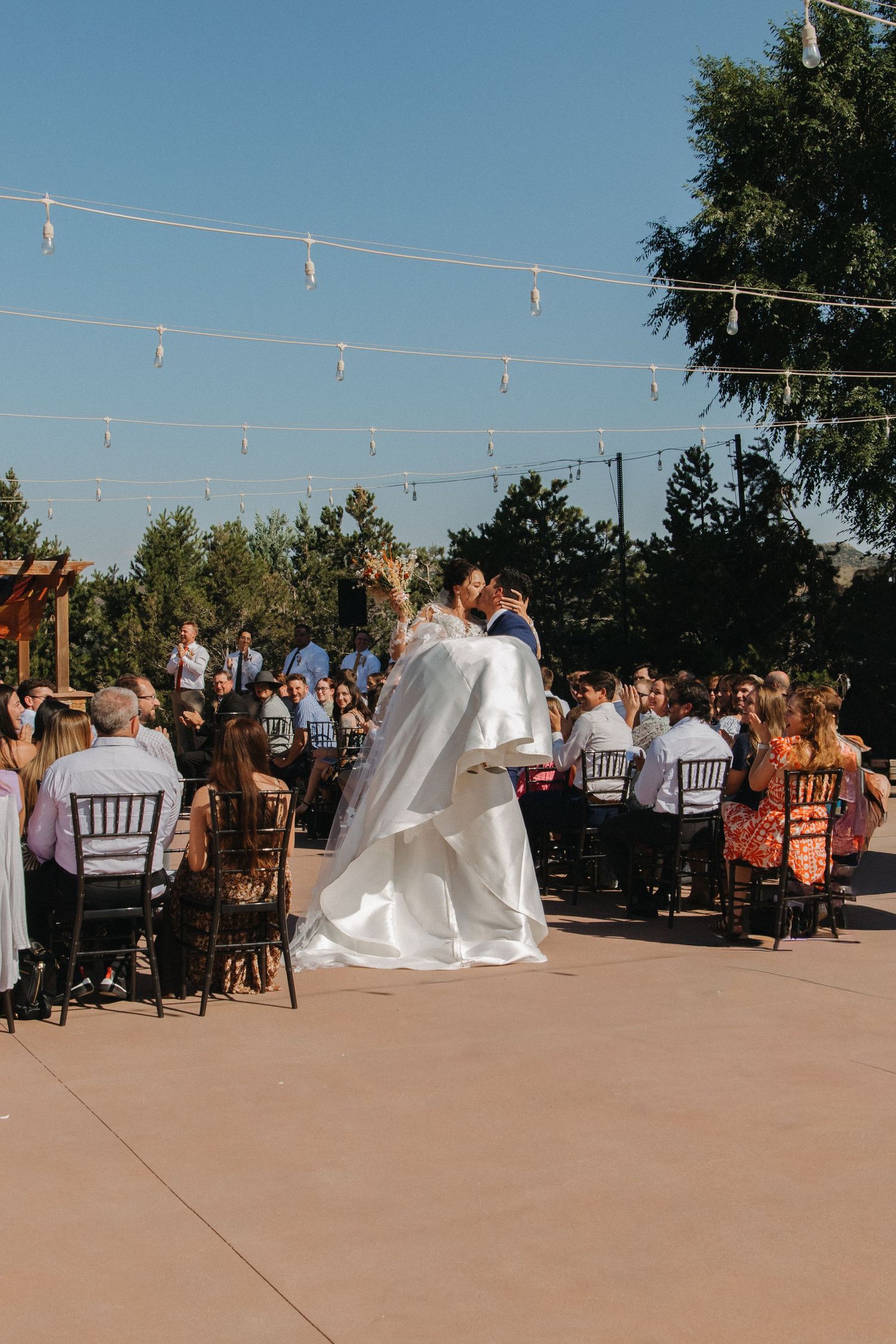 An outdoor wedding reception setup with string lights and guests seated at tables.