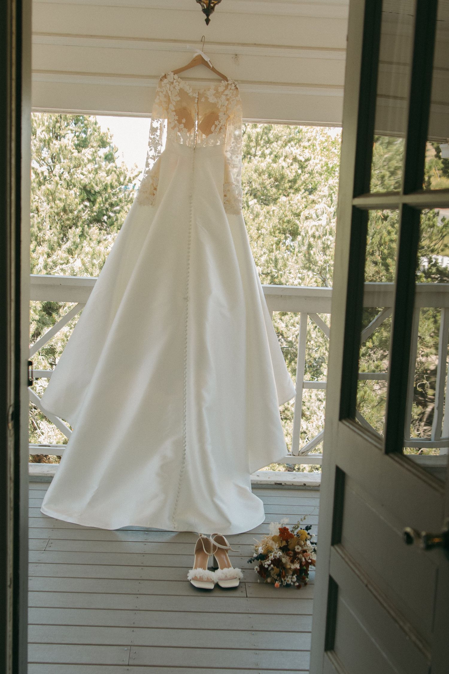 White wedding dresses hanging in a row against white siding with natural light streaming through.