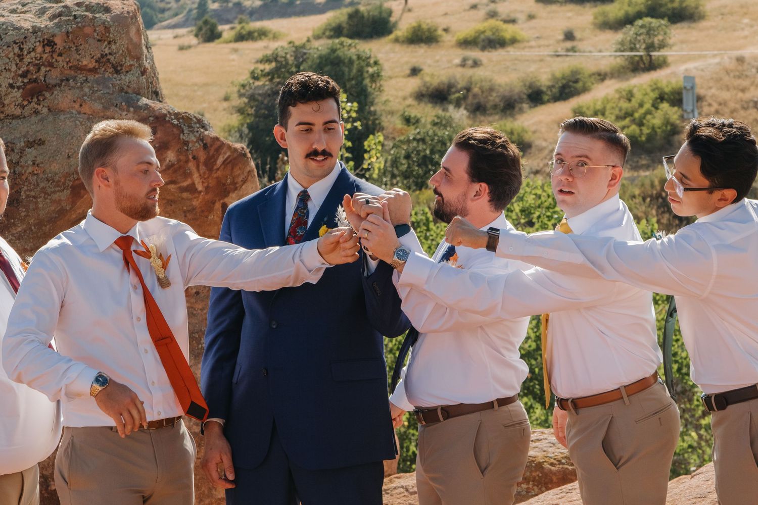 Groomsmen in white shirts and suspenders celebrating outdoors.