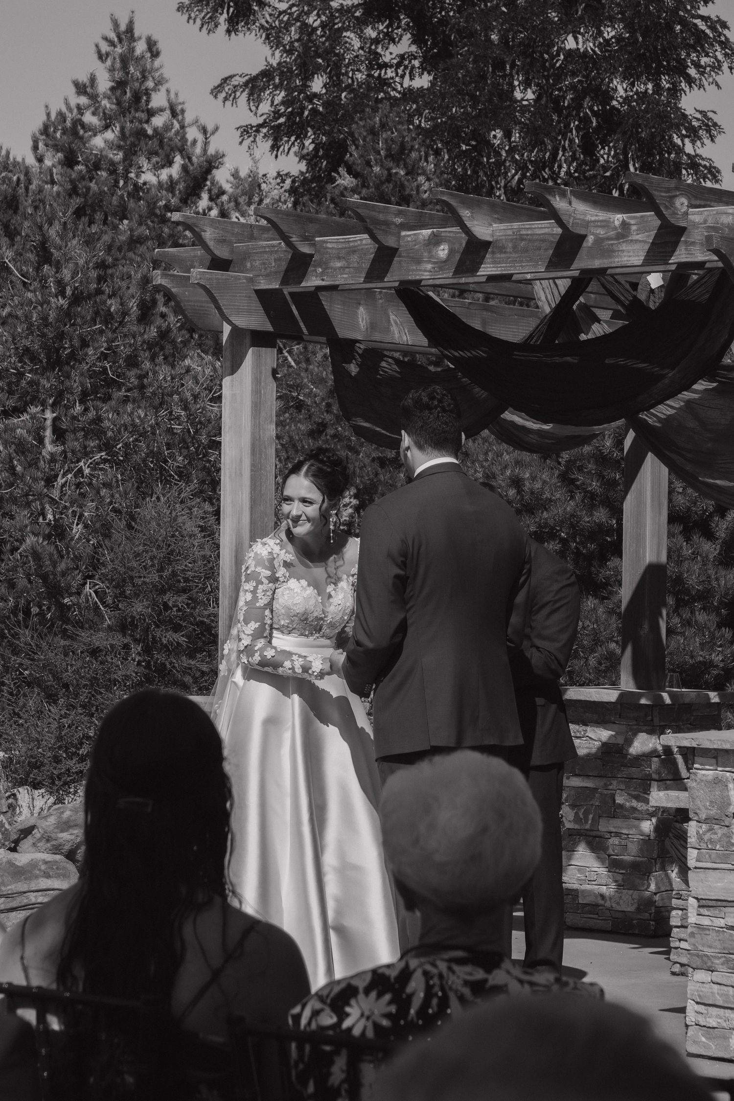 Black and white shot of a wedding ceremony under an outdoor arbor.