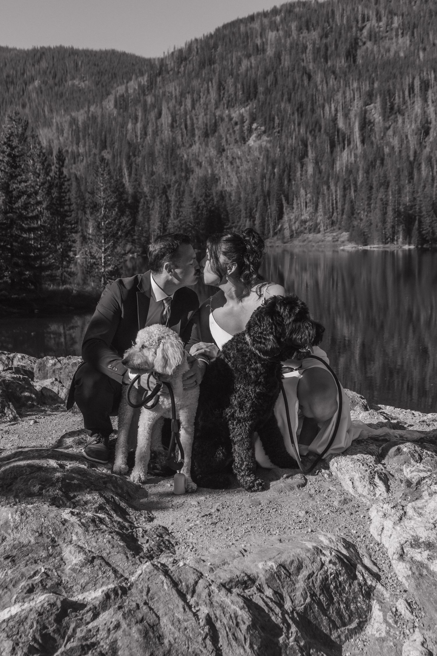 Wedding party sitting on rocky overlook enjoying mountain lake views in black and white.