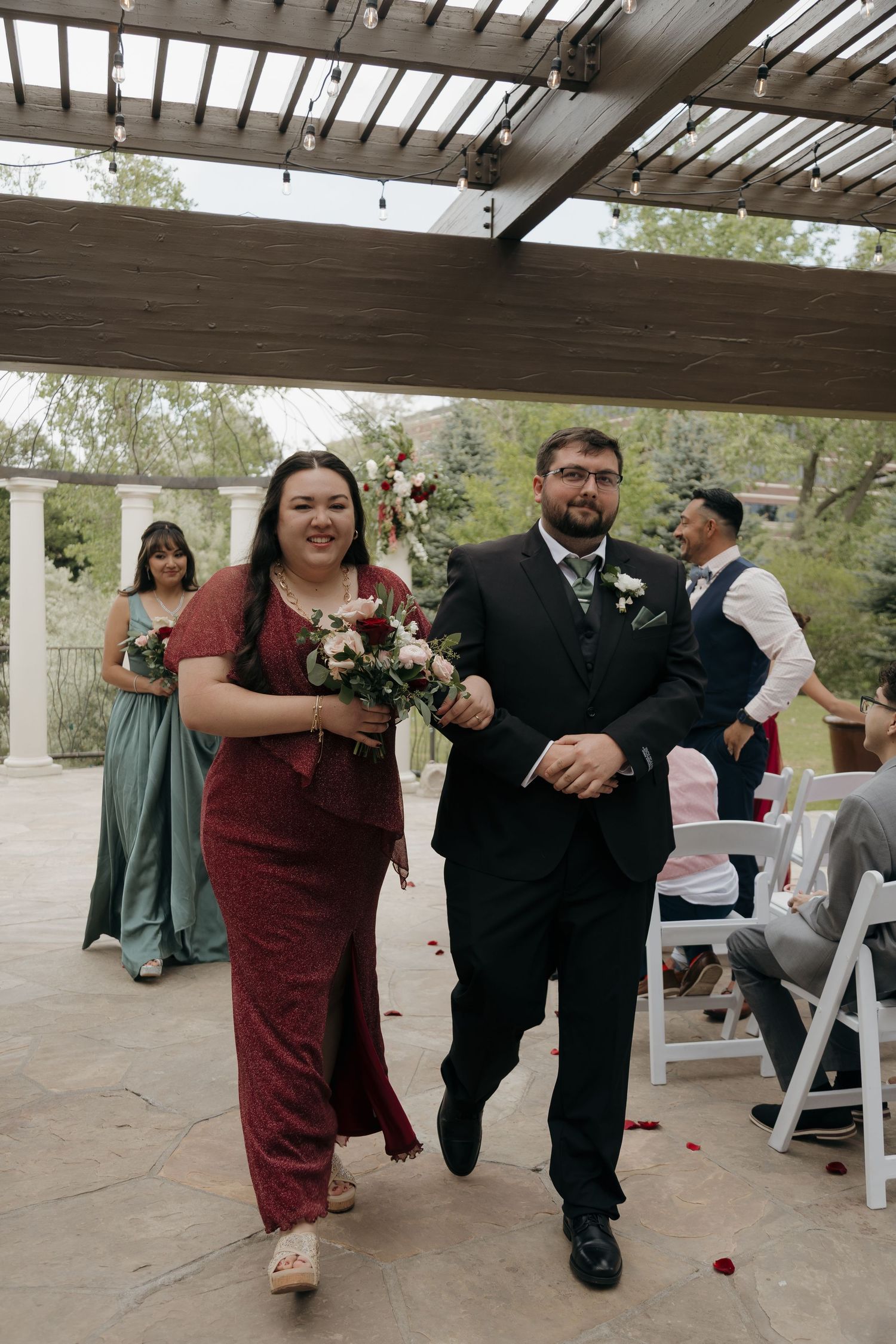 Bridesmaid in red dress walking down the aisle with a groomsman during an outdoor wedding ceremony.