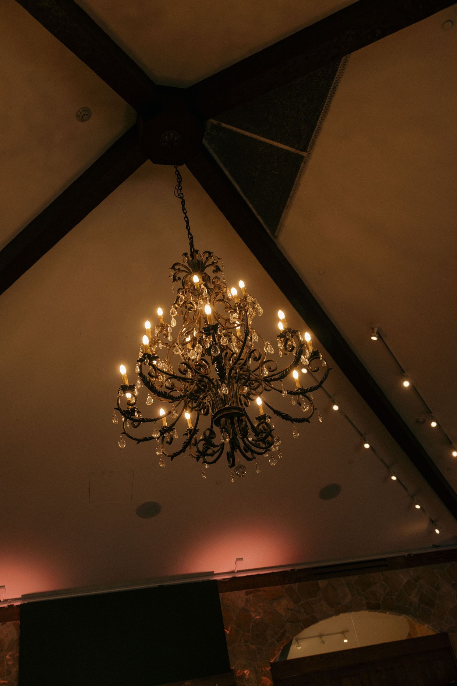 Elegant crystal chandelier hanging from vaulted ceiling with warm ambient lighting.