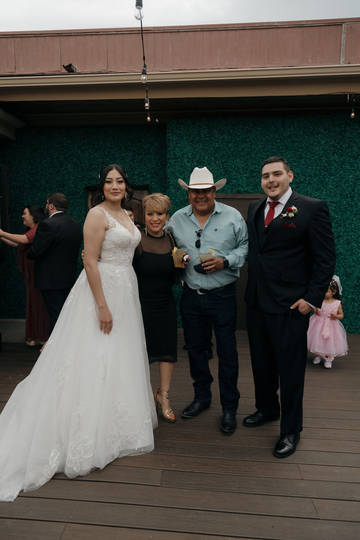 Bride and groom pose with guests including a man in a cowboy hat at an outdoor wedding reception.