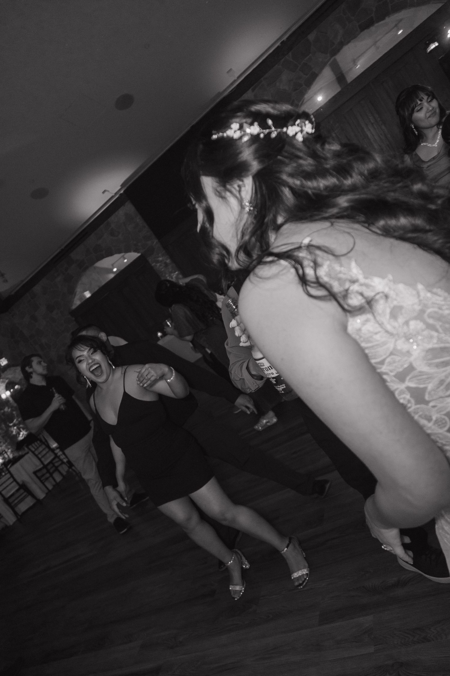 Bride with floral crown dancing energetically with guests on the wedding reception dance floor in black and white.
