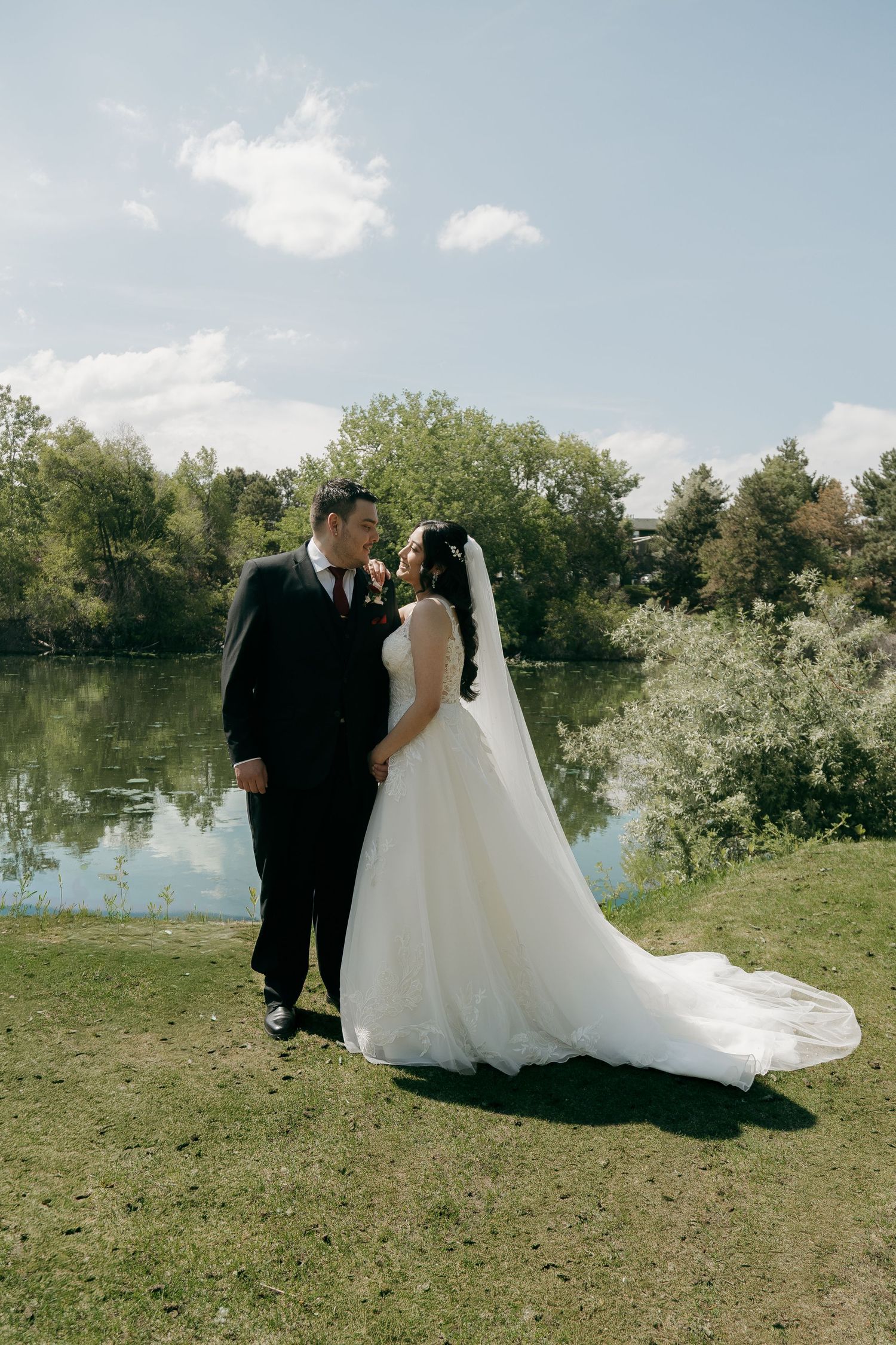 Bride and groom share a romantic moment by a serene lake on their wedding day outdoors.
