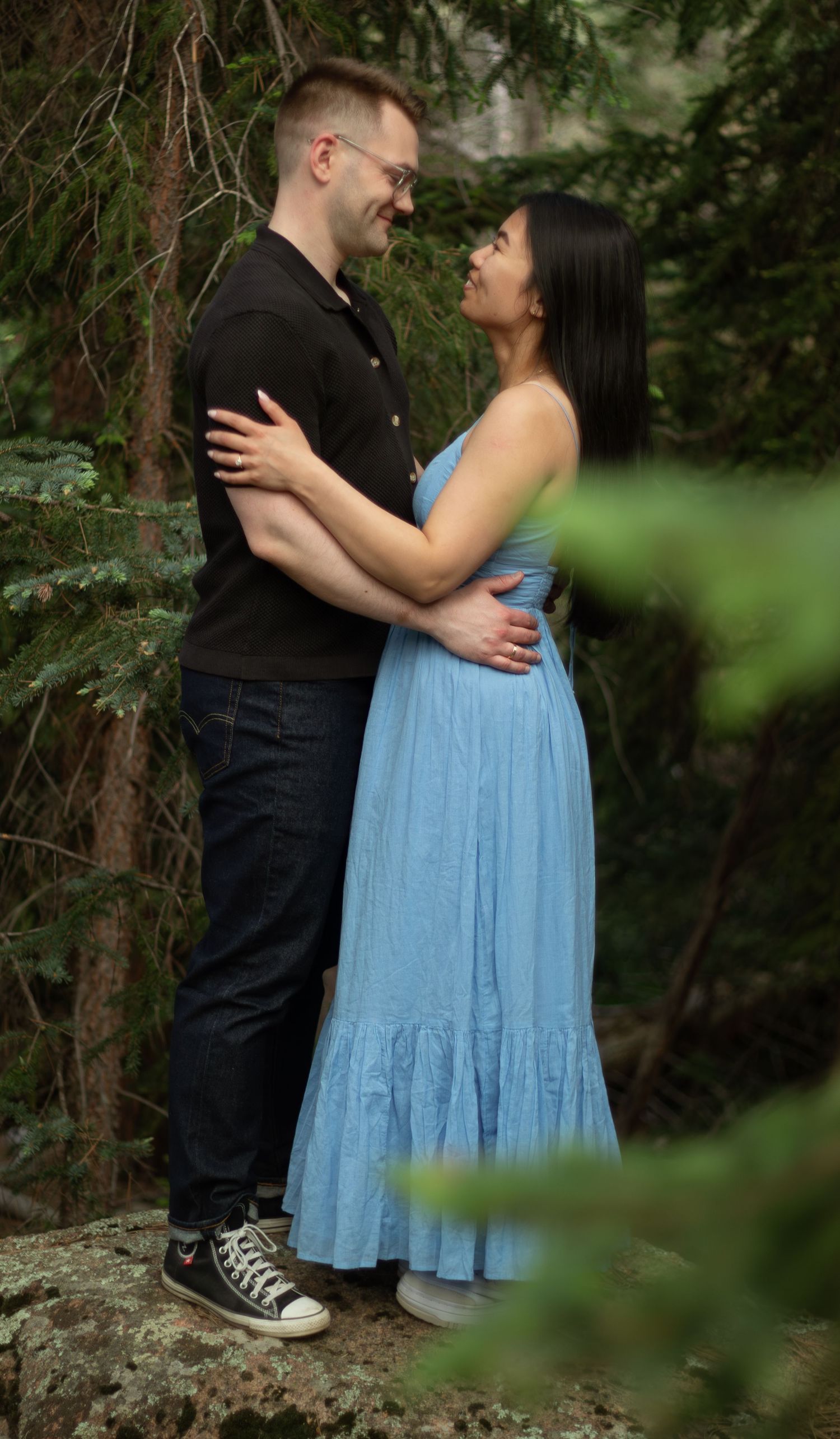A couple embraces on a forest path wearing contrasting black and light blue outfits.