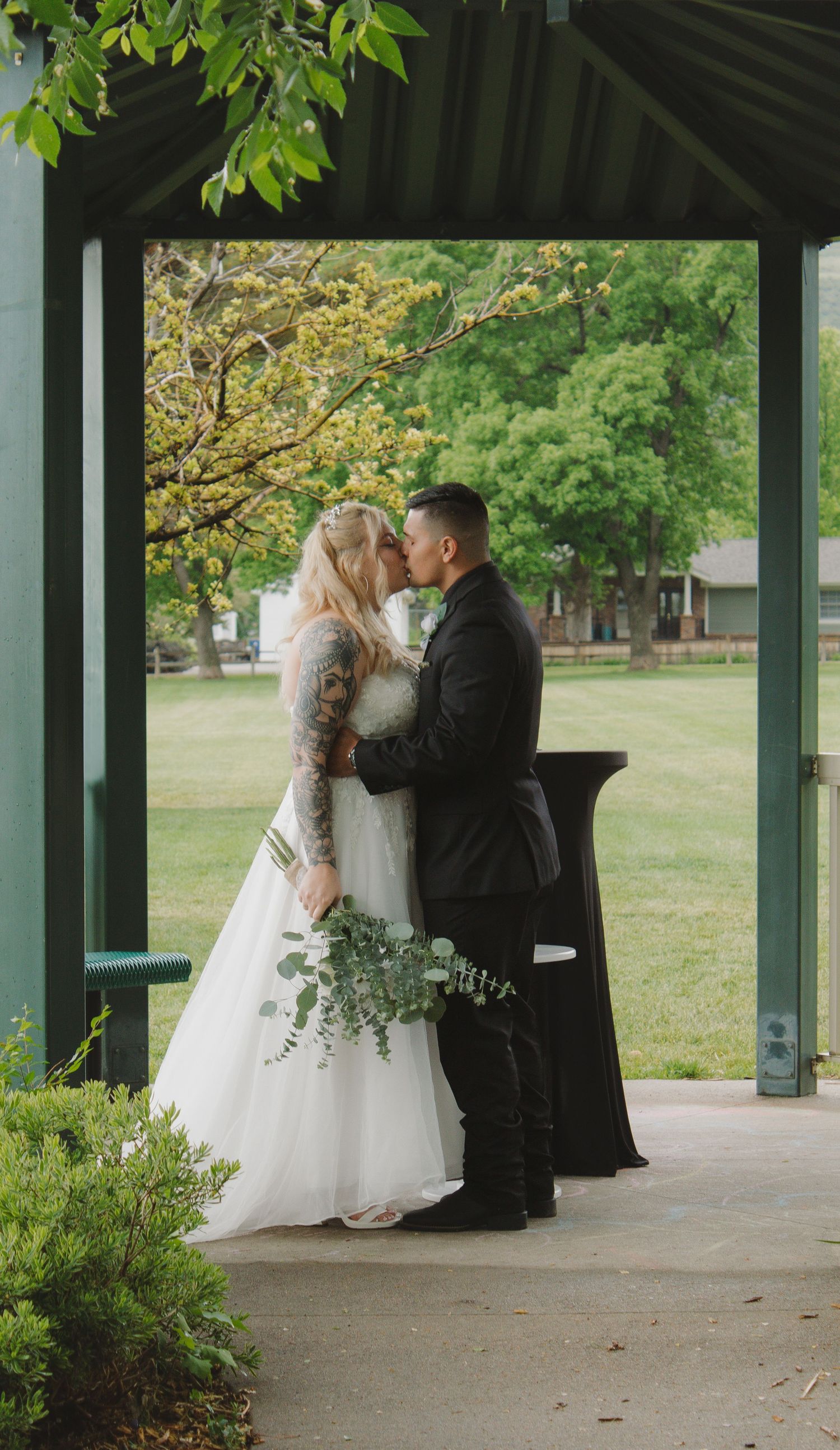 A romantic moment captured during a wedding ceremony in a park pavilion.
