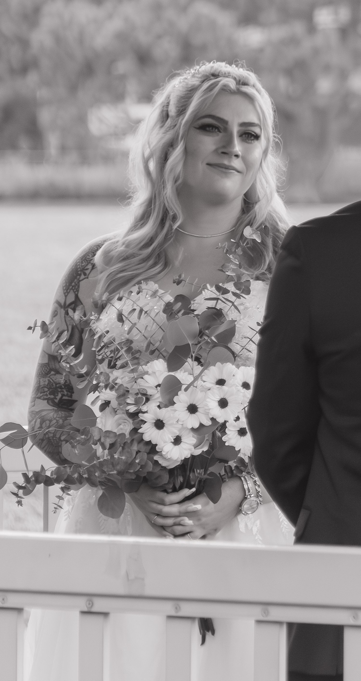 A person in a floral wedding dress holds a bouquet against a white railing.