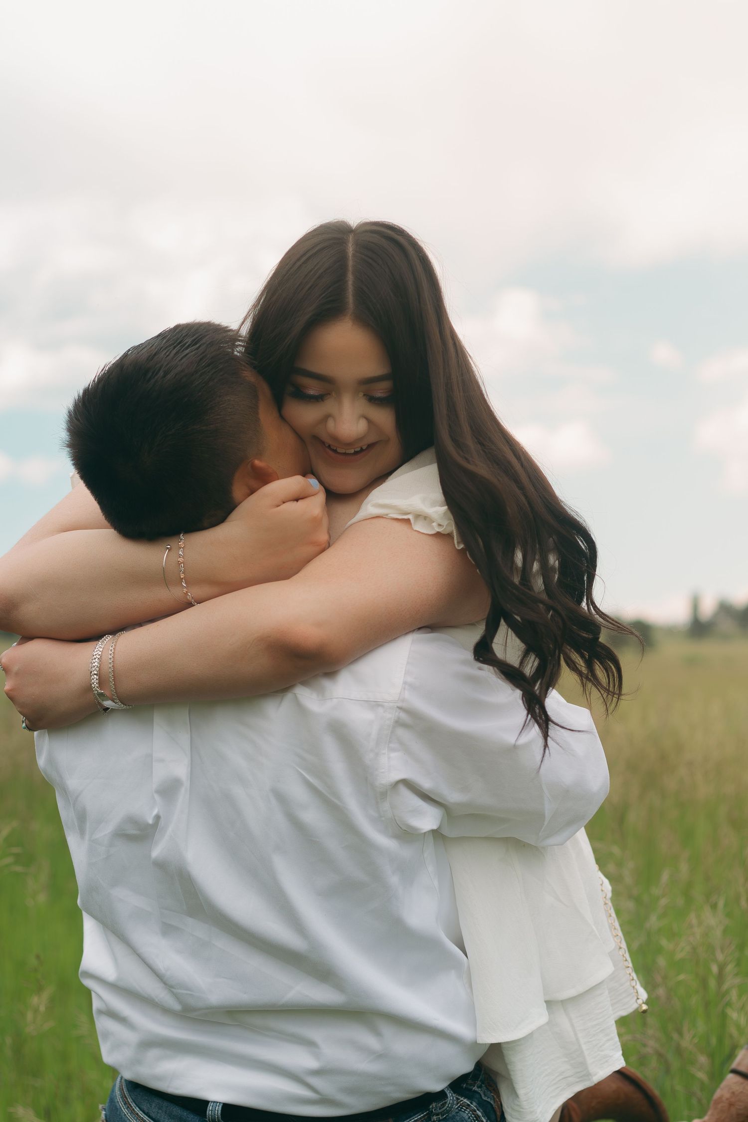 Joyful embrace captured in sunny meadow with mountains in background.