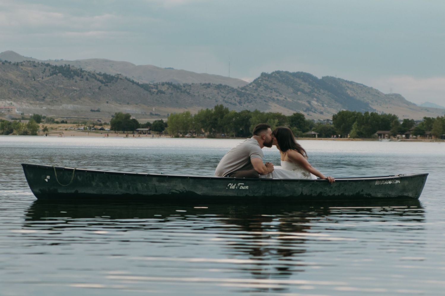 A tender moment between two people in a canoe on a serene lake with mountains in the background.