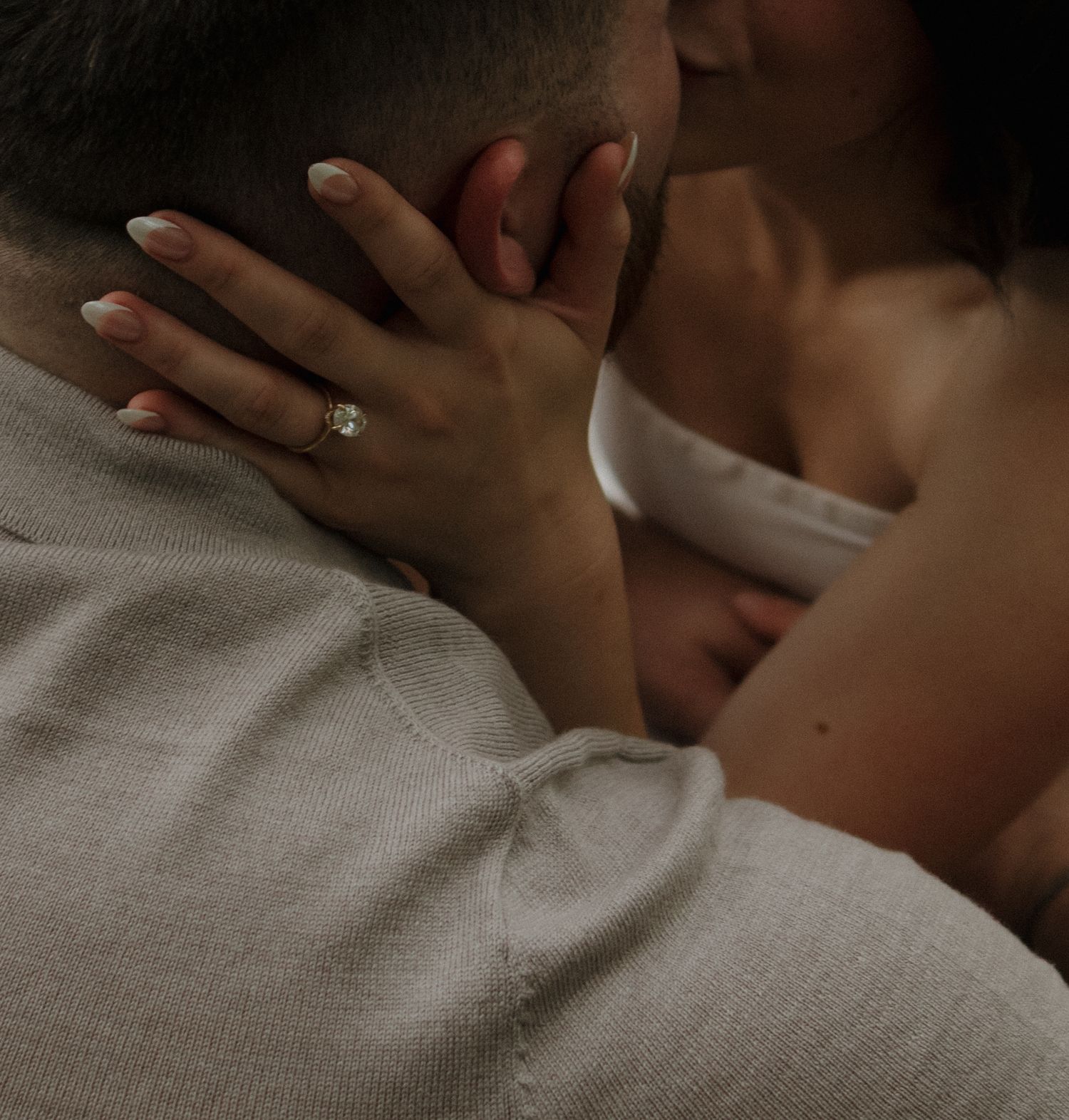 Two hands wearing an engagement ring touch tenderly in a romantic close-up photo.