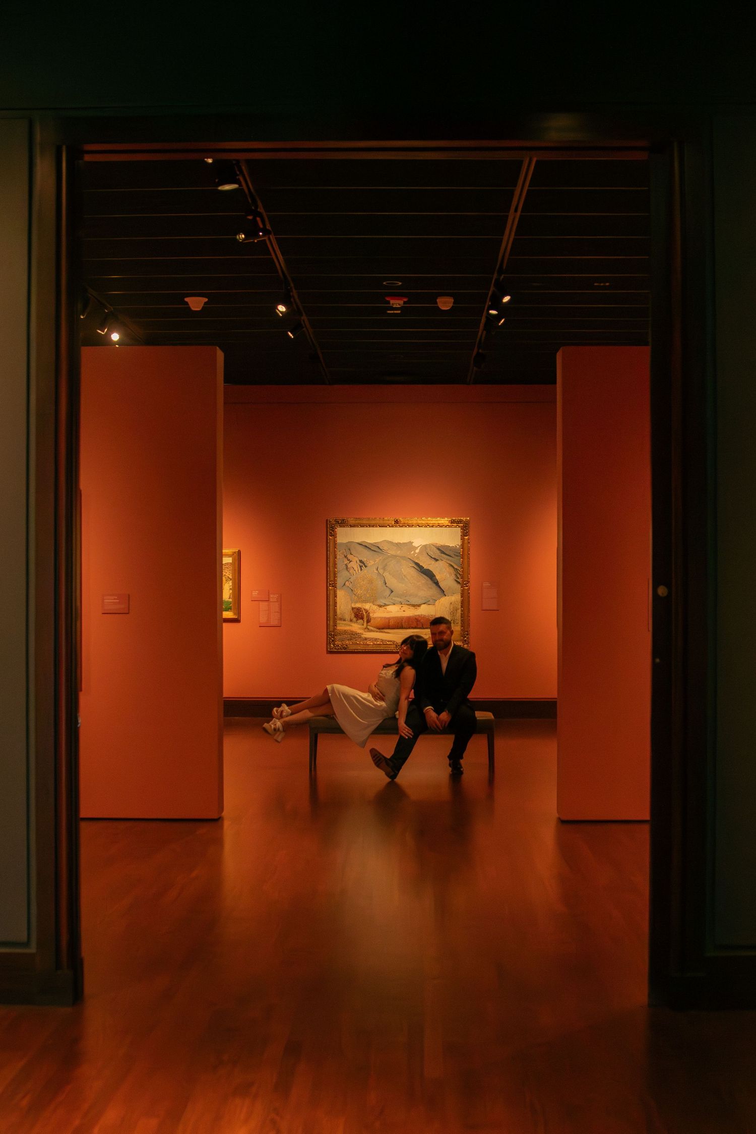 Art gallery interior with orange walls and hardwood floors in dramatic lighting.