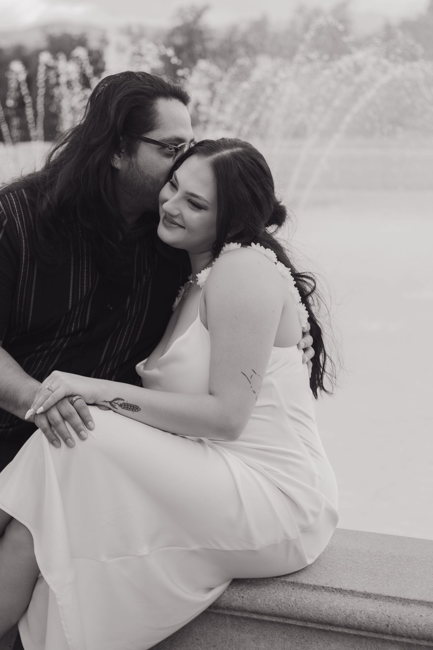 A romantic black and white photo of a couple sharing an intimate moment by a fountain.