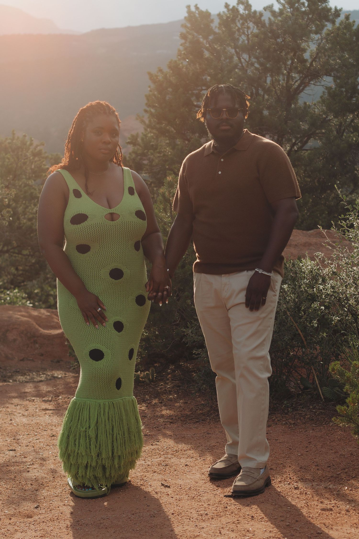 Couple in romantic sunset photoshoot with one wearing lime green polka dot dress and other in white pants.