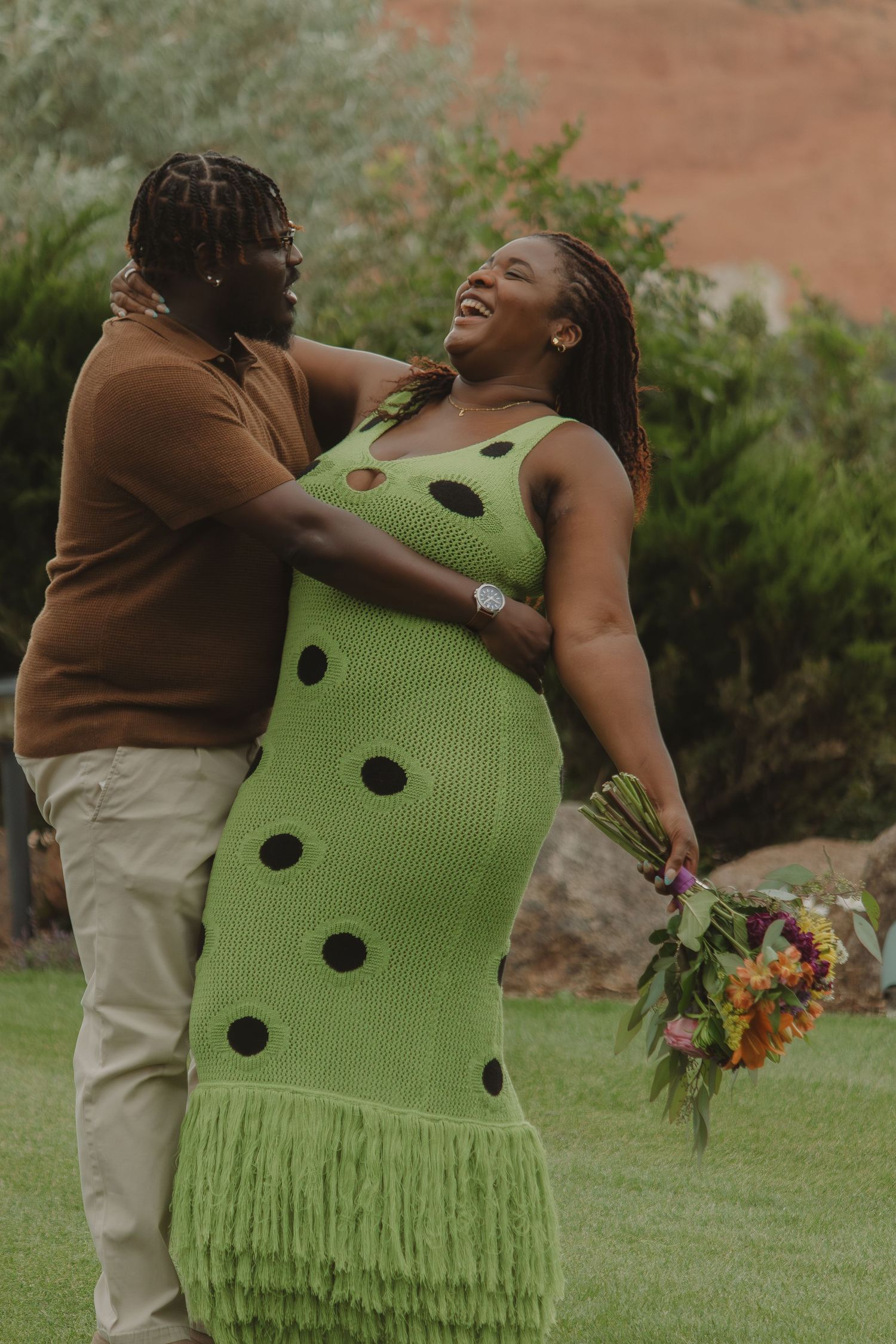 A sweet outdoor couple's photoshoot showing joyful laughter against greenery in semi-casual attire.