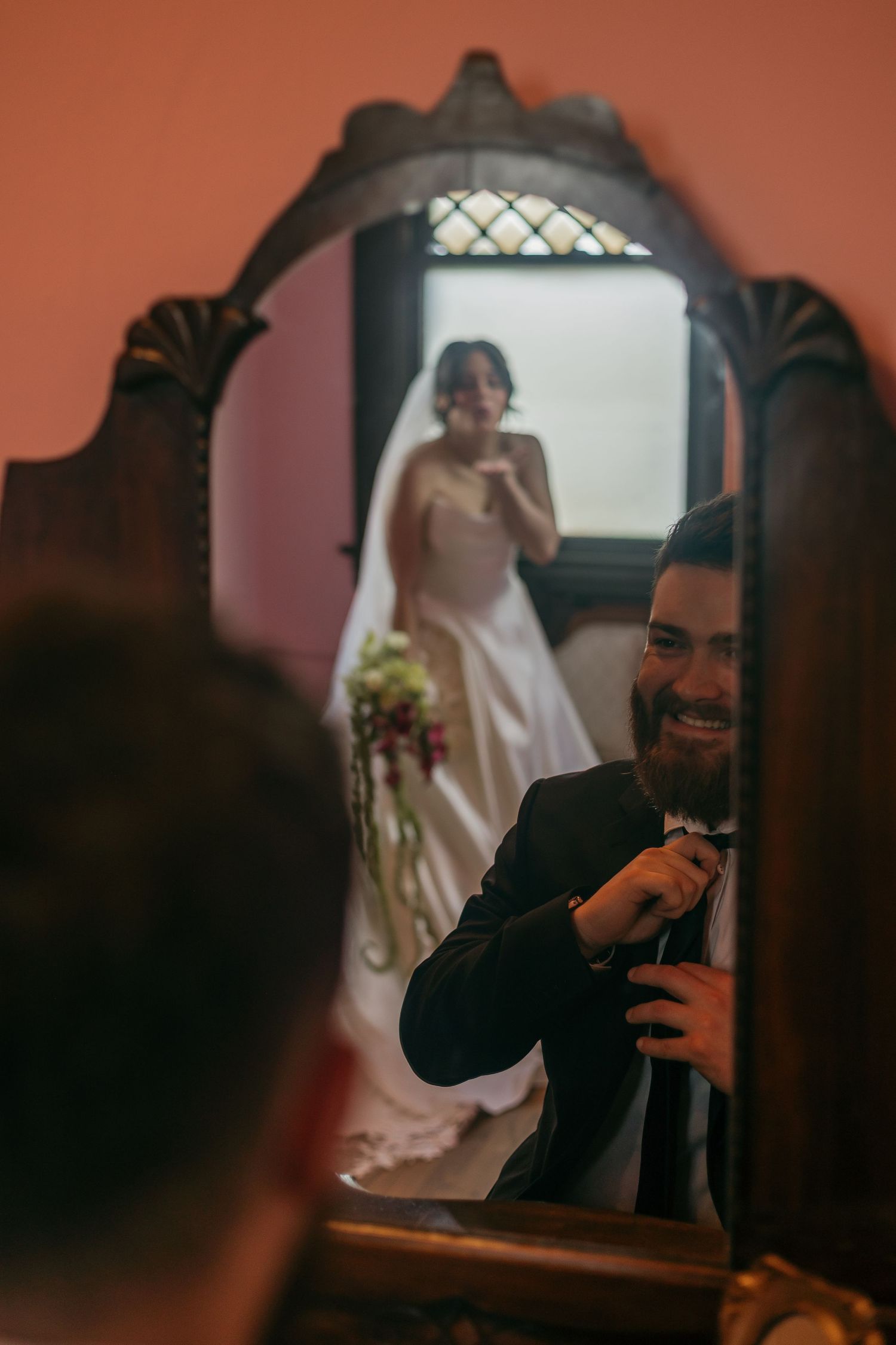 A mirror reflection captures a wedding moment with a bride in white and someone taking a photo through an ornate frame.