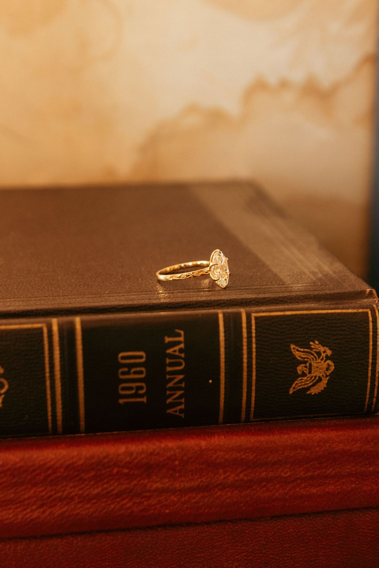 Diamond engagement ring placed on vintage leather-bound book in warm lighting.