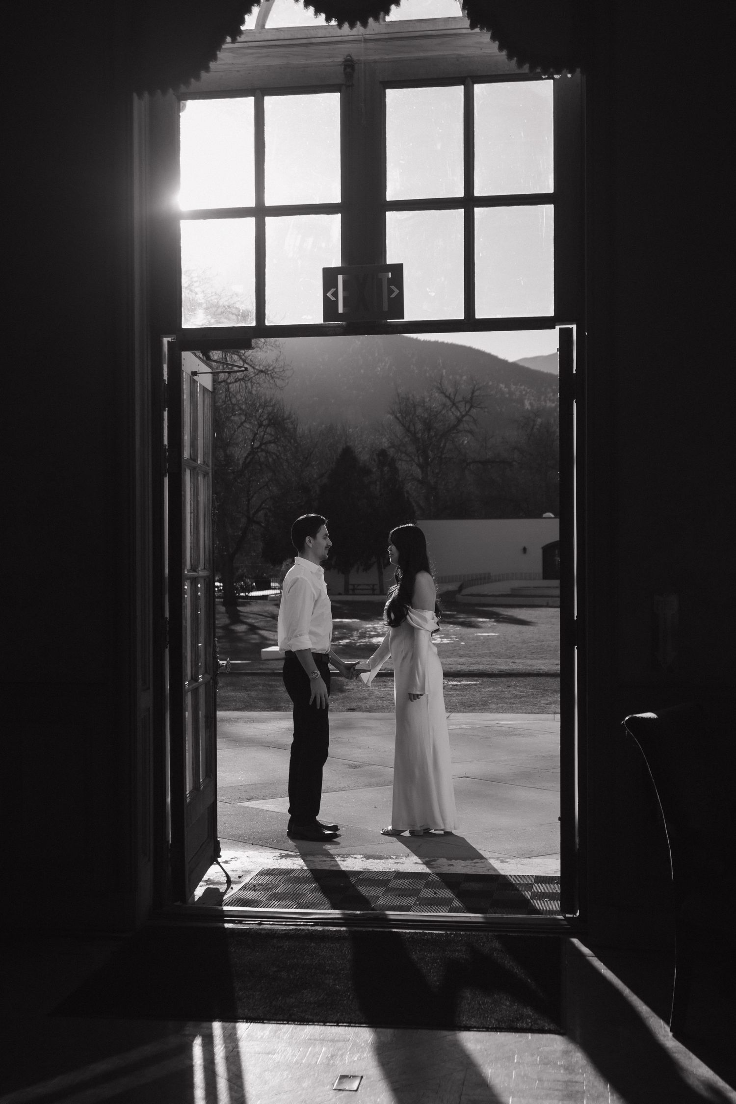 Silhouetted couple standing in a doorway against bright natural light and mountain backdrop.
