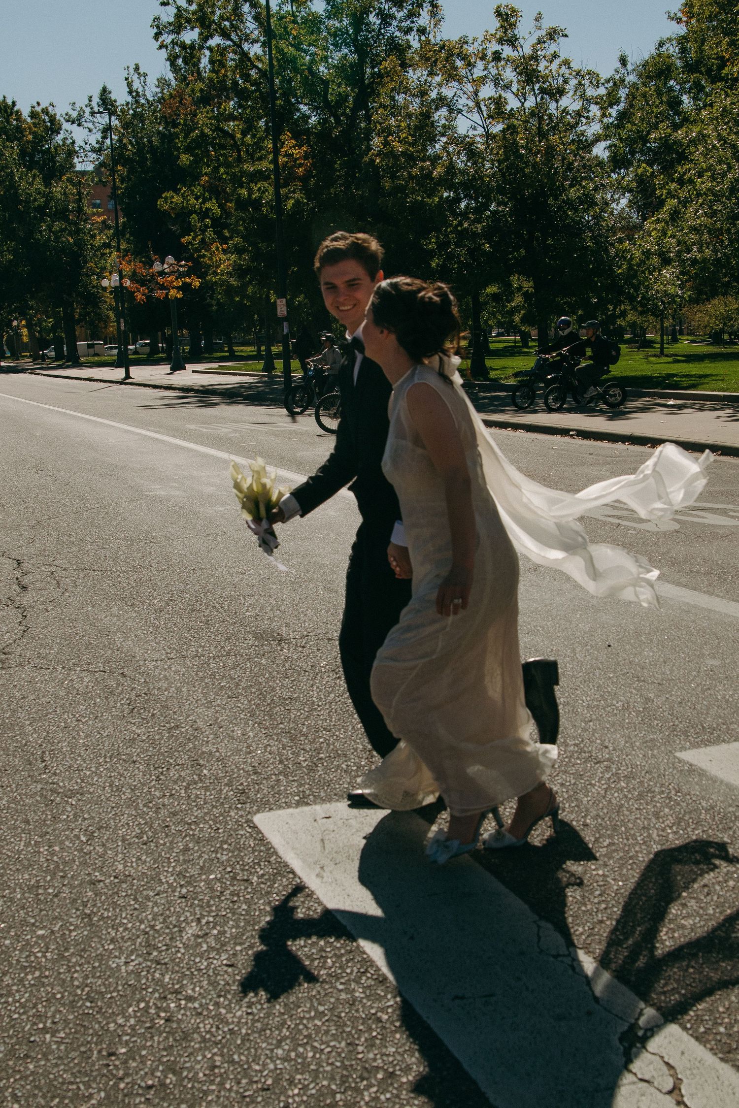 Couple walking on a sunny street with flowing dress and casting shadows.
