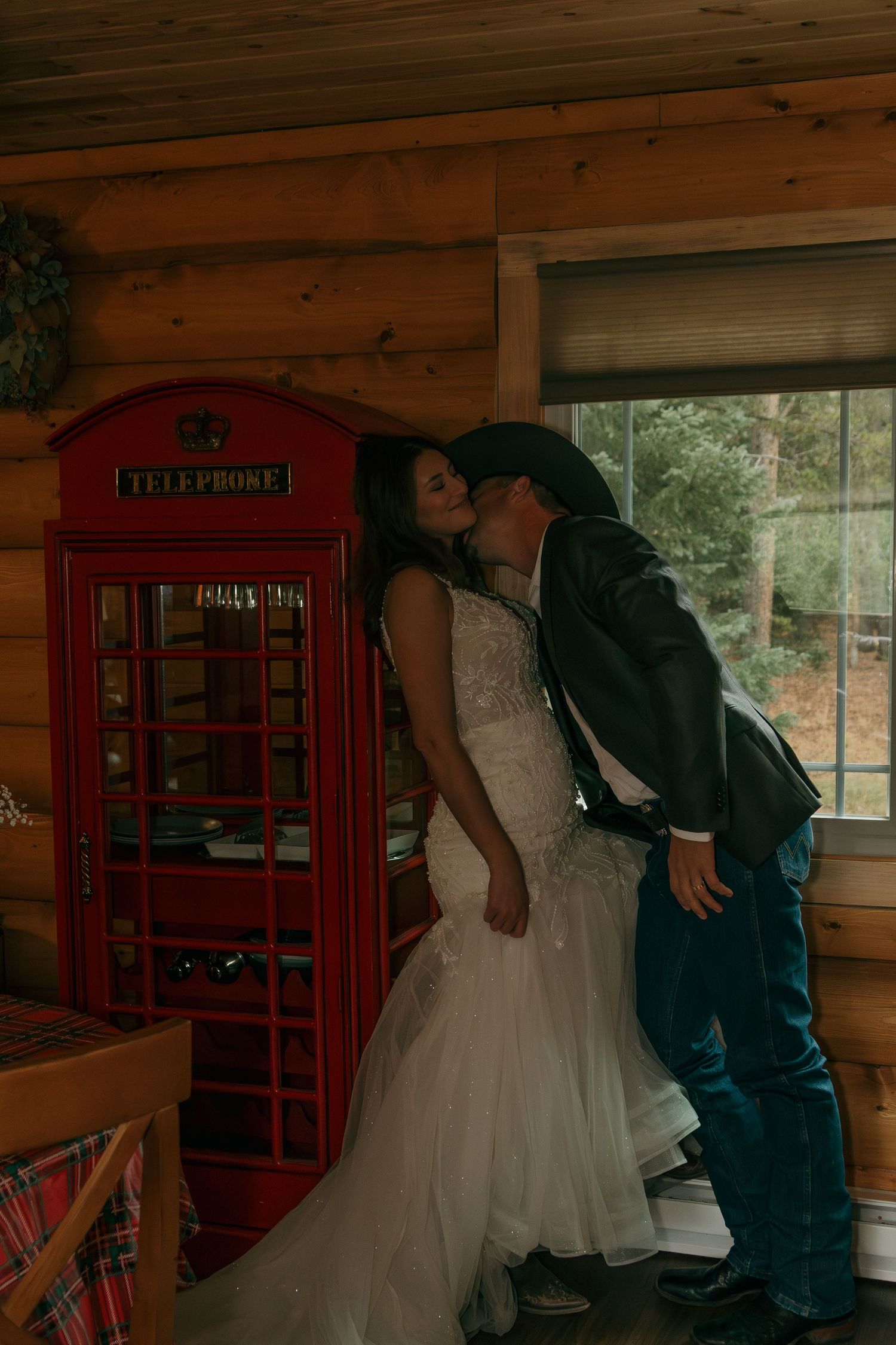 A romantic moment by a red British phone booth inside a cozy wooden cabin.