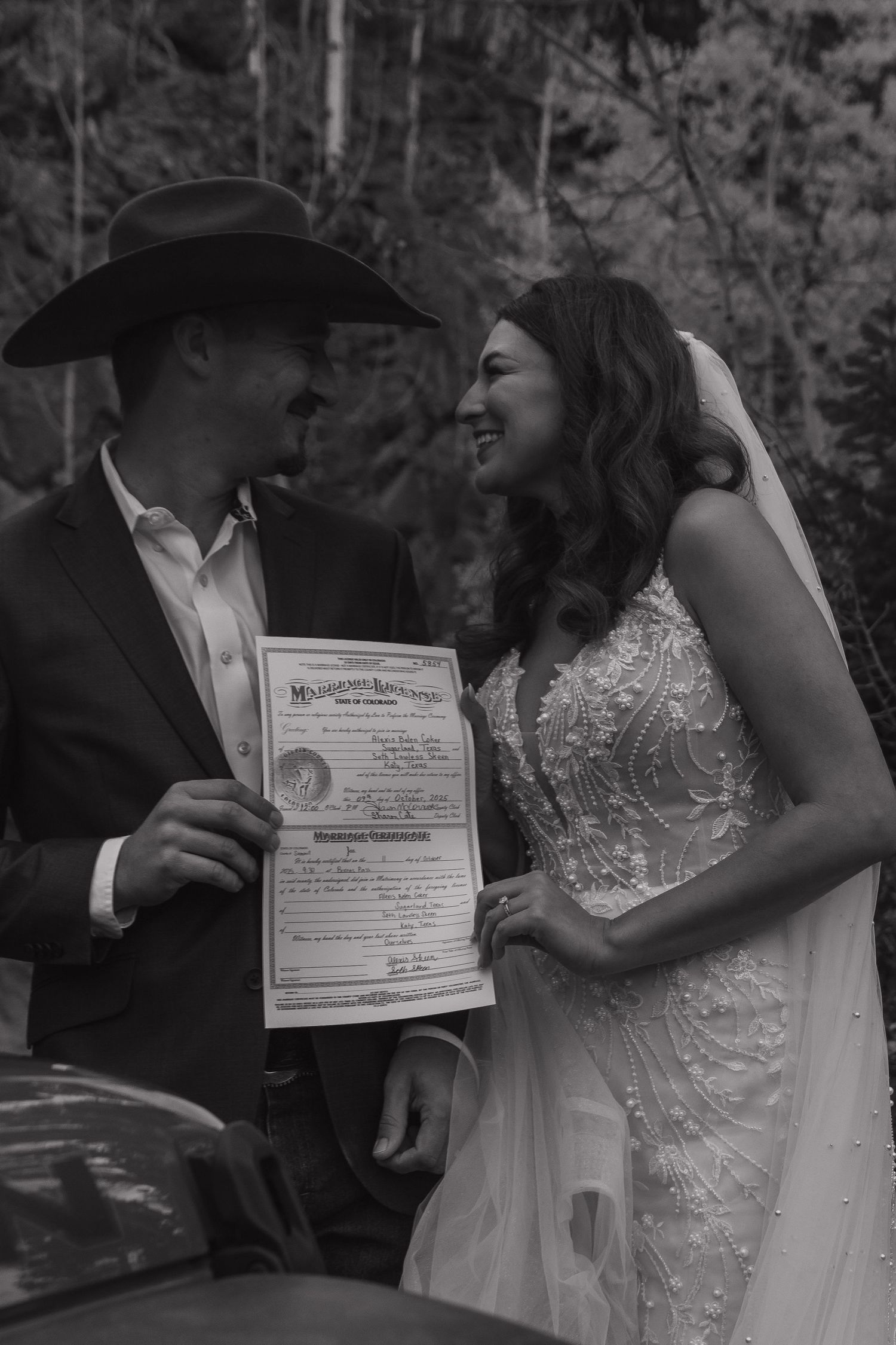 A black and white photo of a couple signing their marriage certificate during an outdoor ceremony.