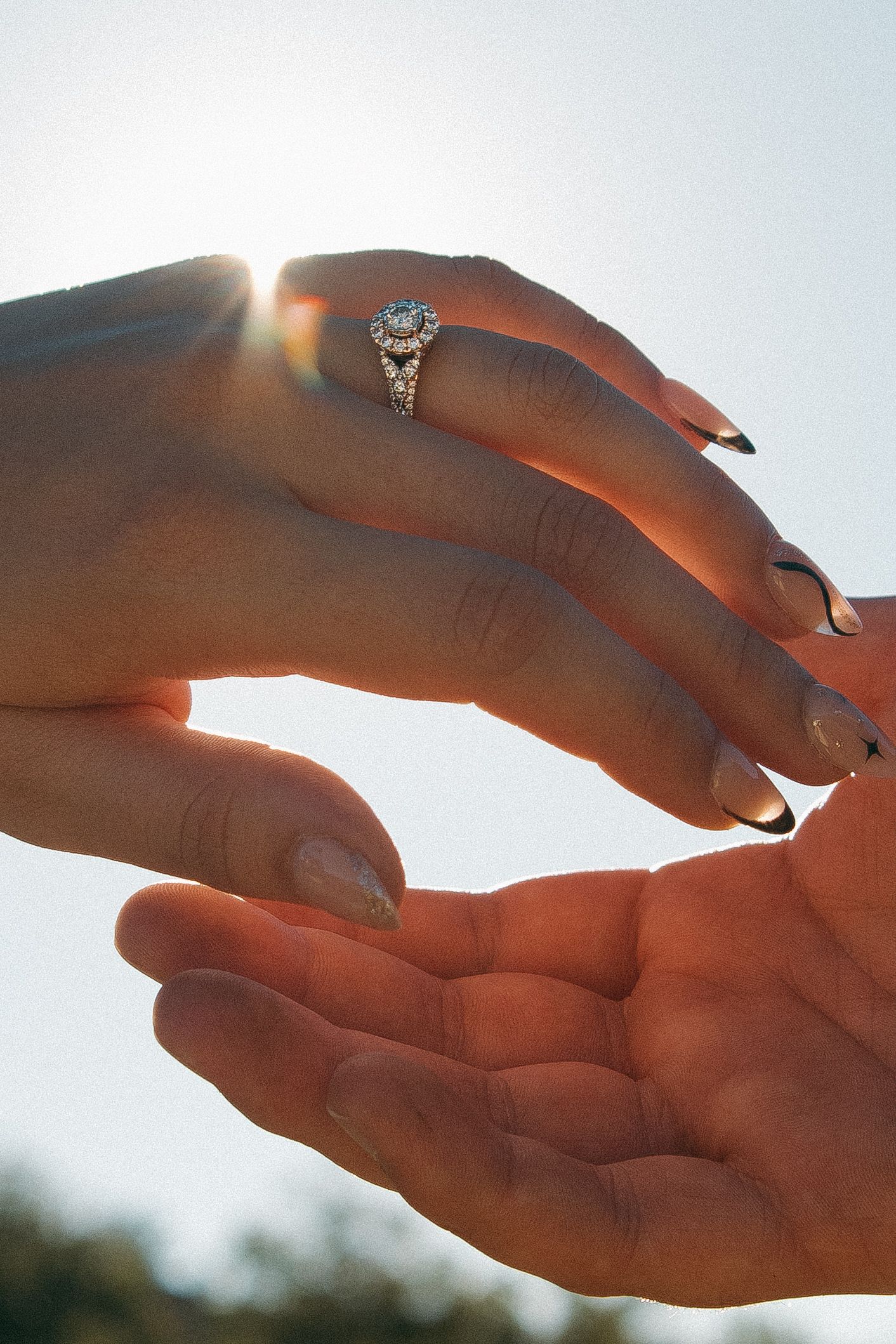 A hand silhouetted against the bright sun holds up a small ring, creating a lens flare effect in the sky.