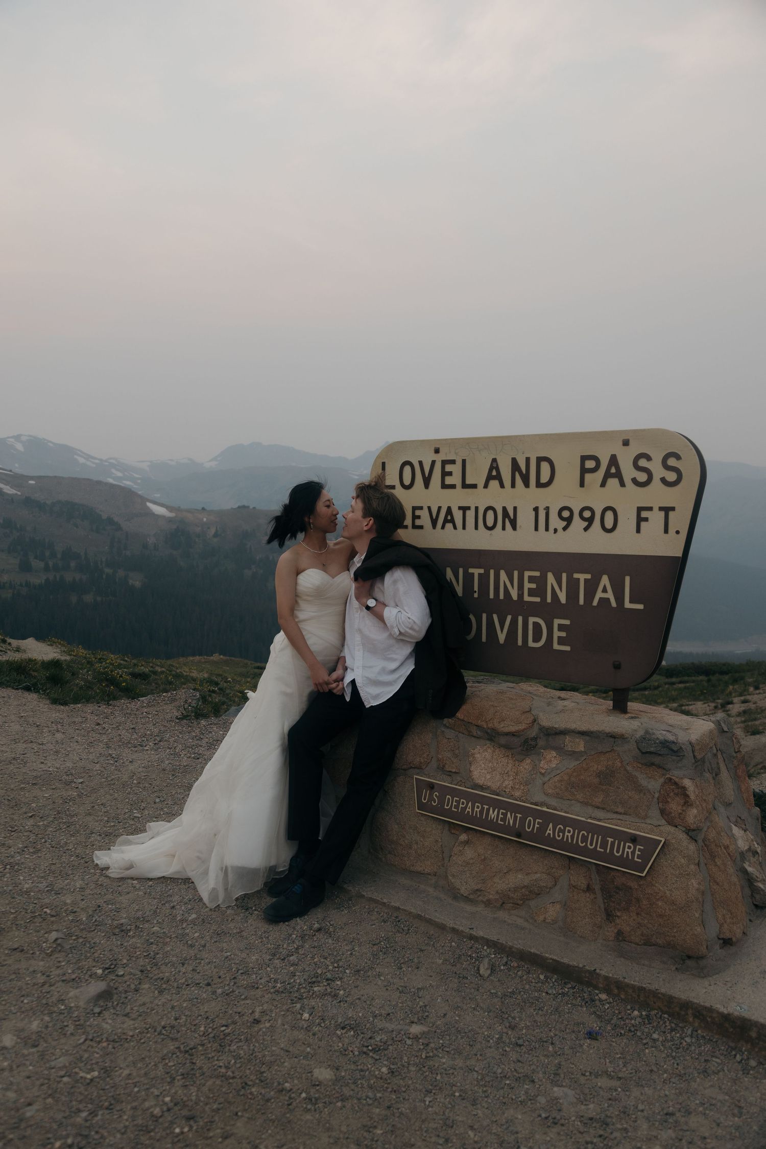 Couple in wedding attire kiss beside Loveland Pass Continental Divide sign at elevation 11,990 feet.