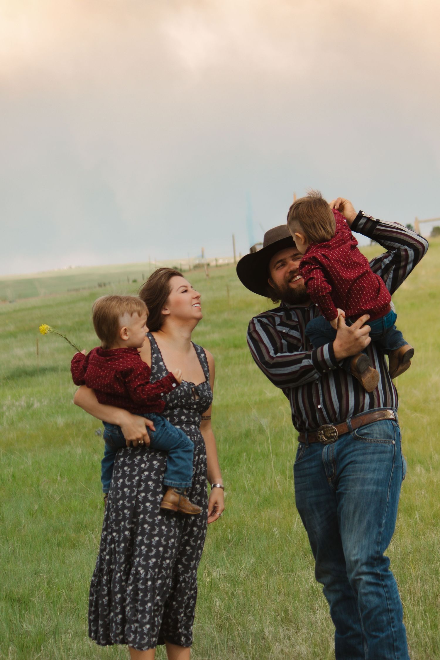 Family playfully lifts children in the air against sunset sky in grassy field.