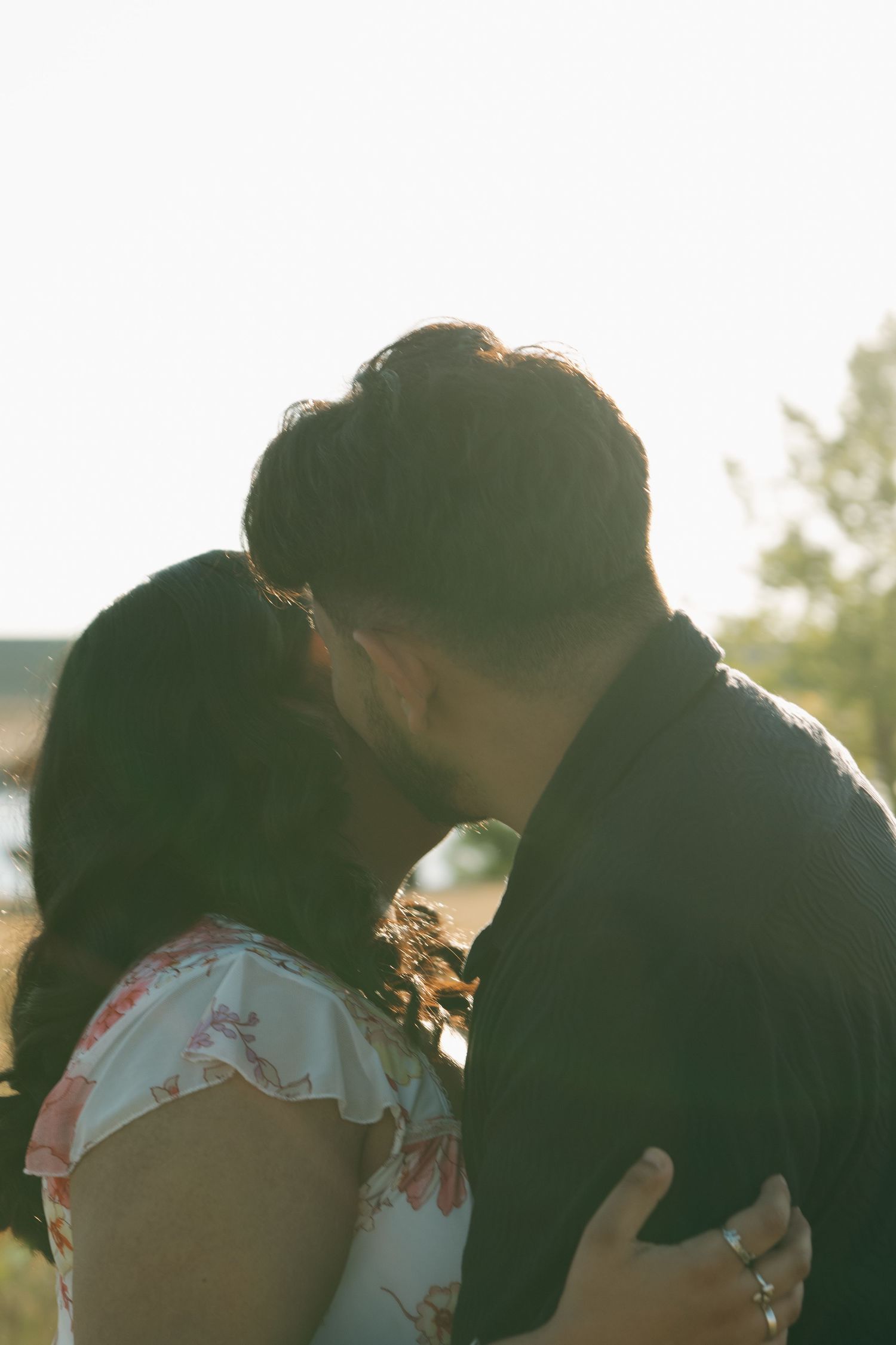 A romantic couple shares an intimate moment backlit by warm sunlight in a grassy field.