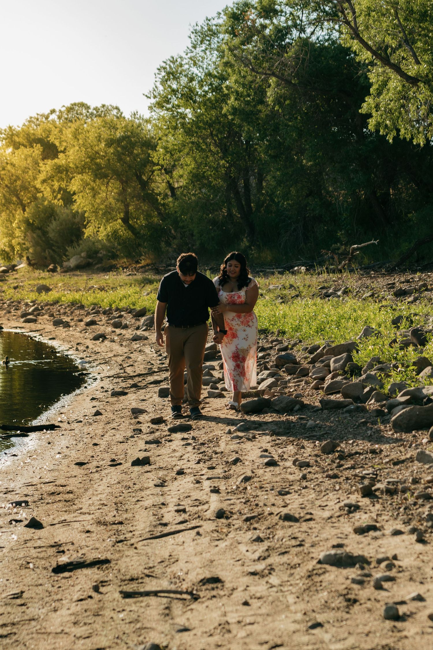 Couple walking along a rocky riverbank during golden hour.