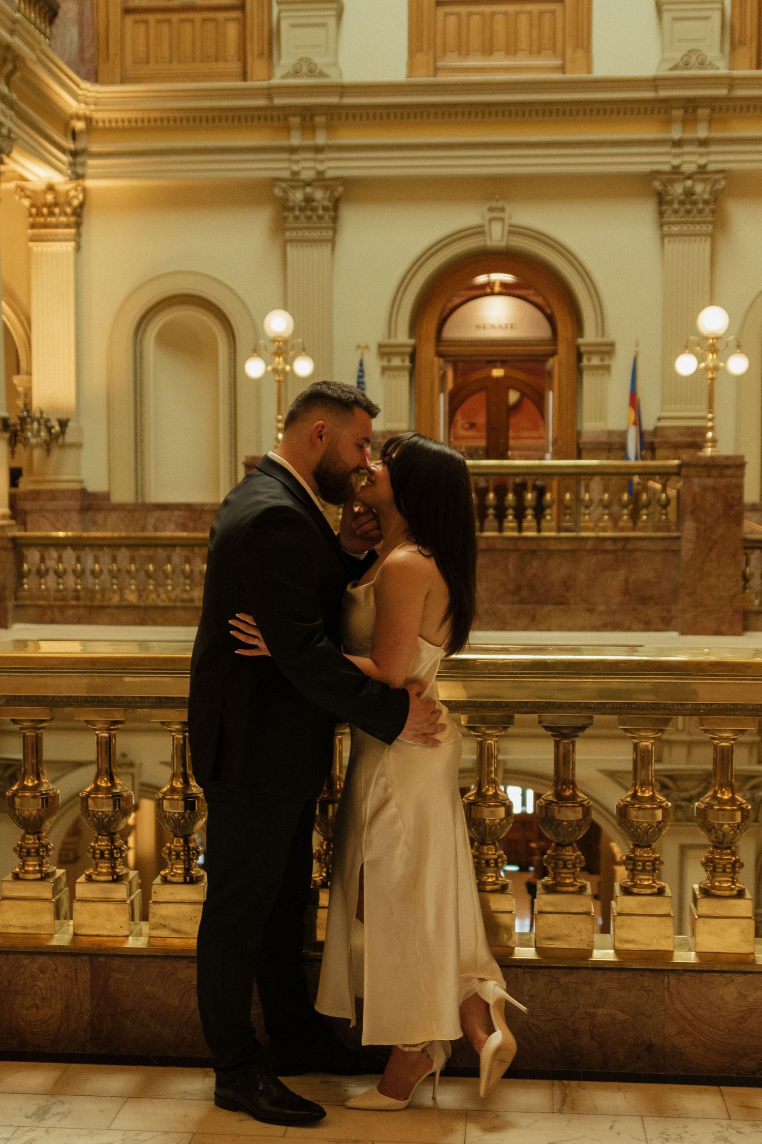 A romantic moment captured on an ornate marble staircase with elegant vintage architecture and warm lighting.