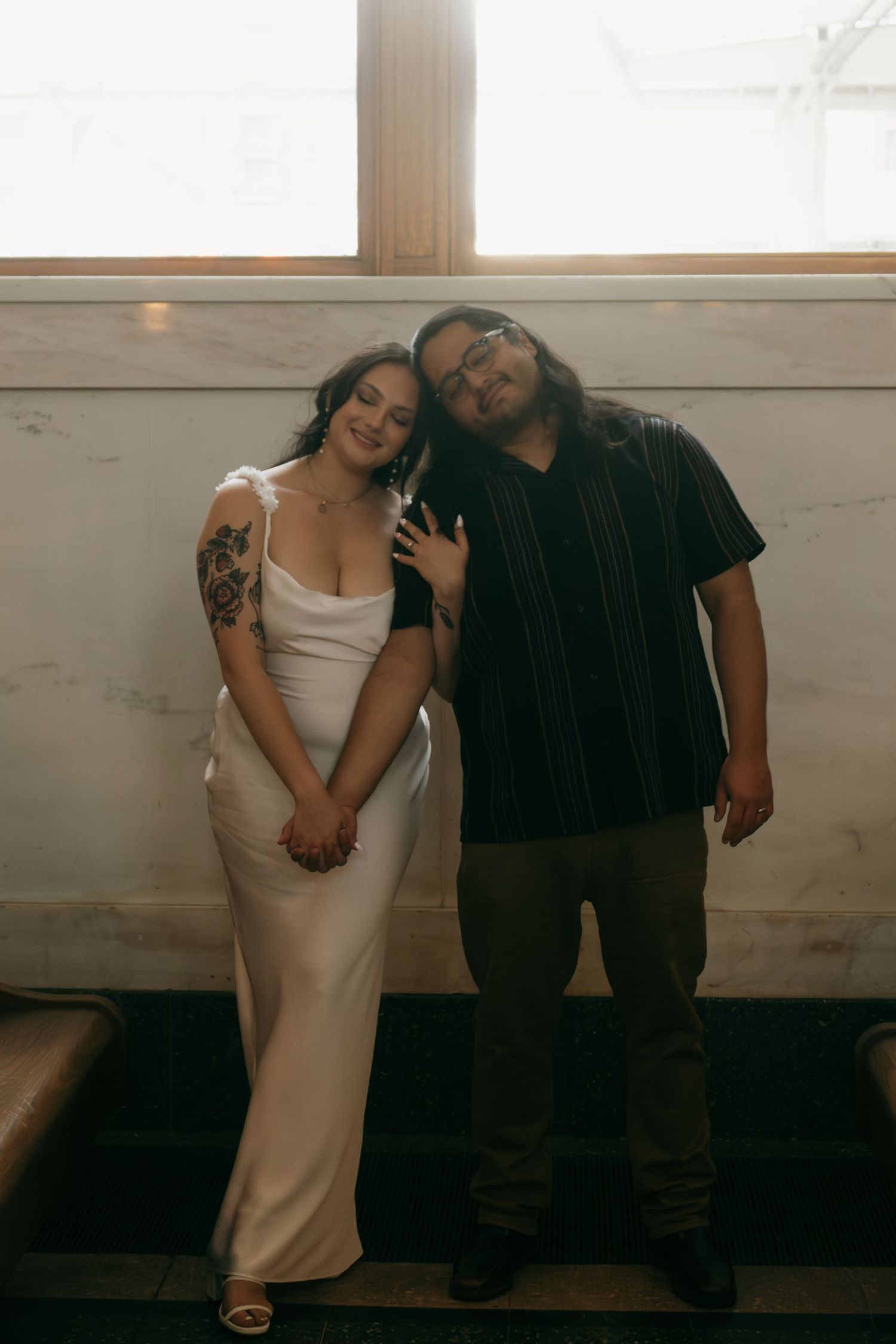 Couple shares playful moments against white wall during indoor photo session.