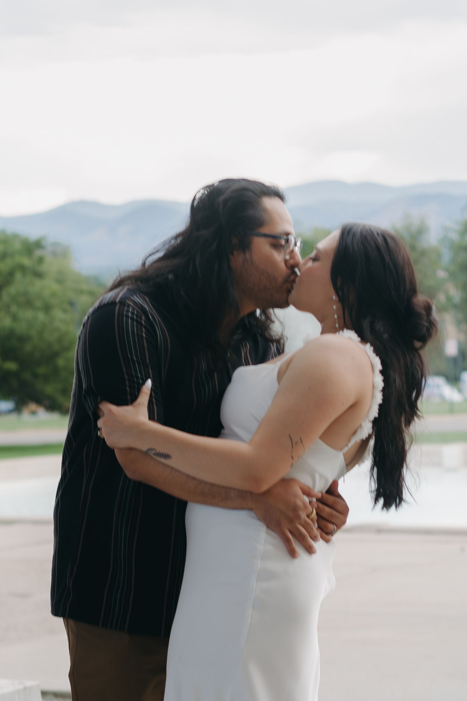 A couple embraces outdoors with mountain scenery in the background.
